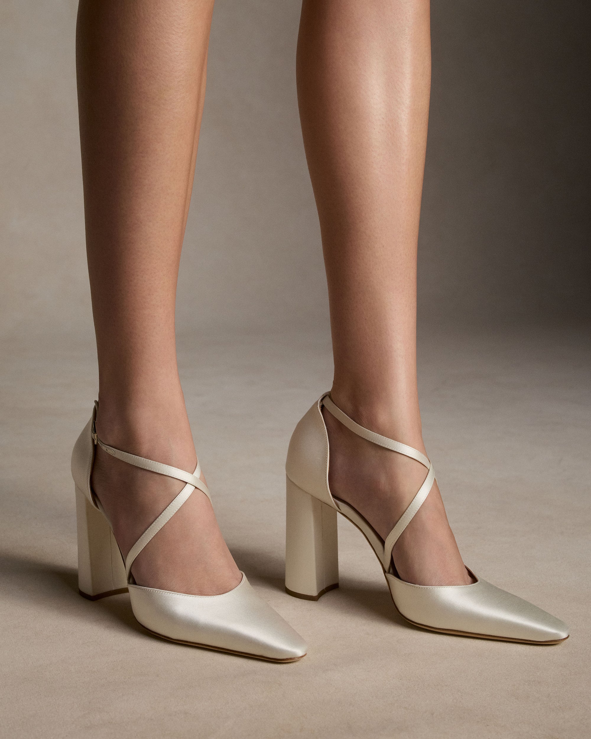 Classic rounded square toe pump with criss cross ankle strap, crafted in Italy of ivory satin. 100mm block heel.
