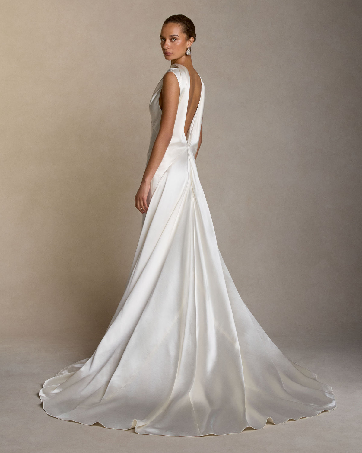 Silk wool bias cut V neck gown. Straps peel away at shoulders, intertwining with a neck drape that falls into an open deep V at back. Diagonal seam detail at center back skirt releases into full train. Invisible zip closure at center back. 