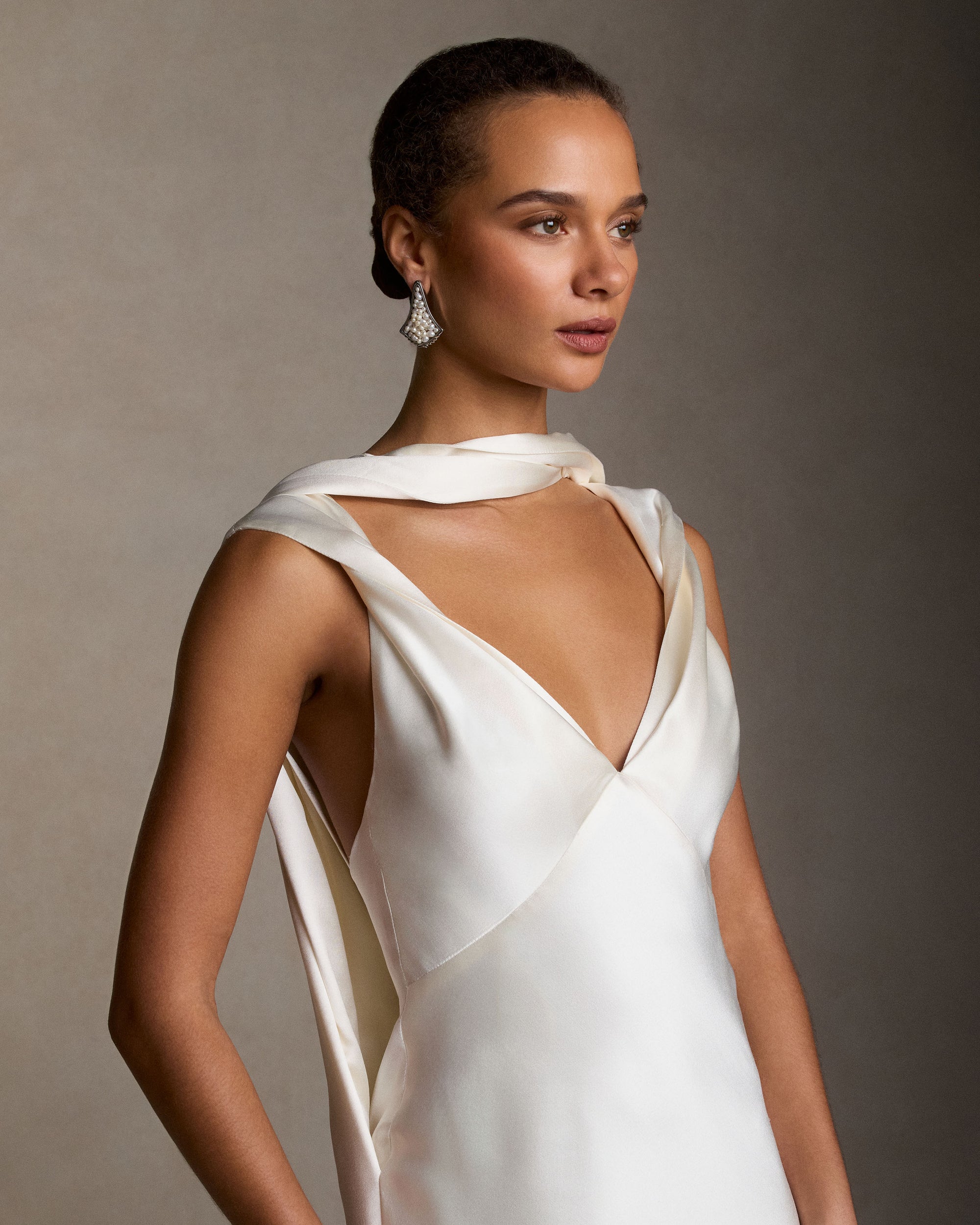 Silk wool bias cut V neck gown. Straps peel away at shoulders, intertwining with a neck drape that falls into an open deep V at back. Diagonal seam detail at center back skirt releases into full train. Invisible zip closure at center back. 