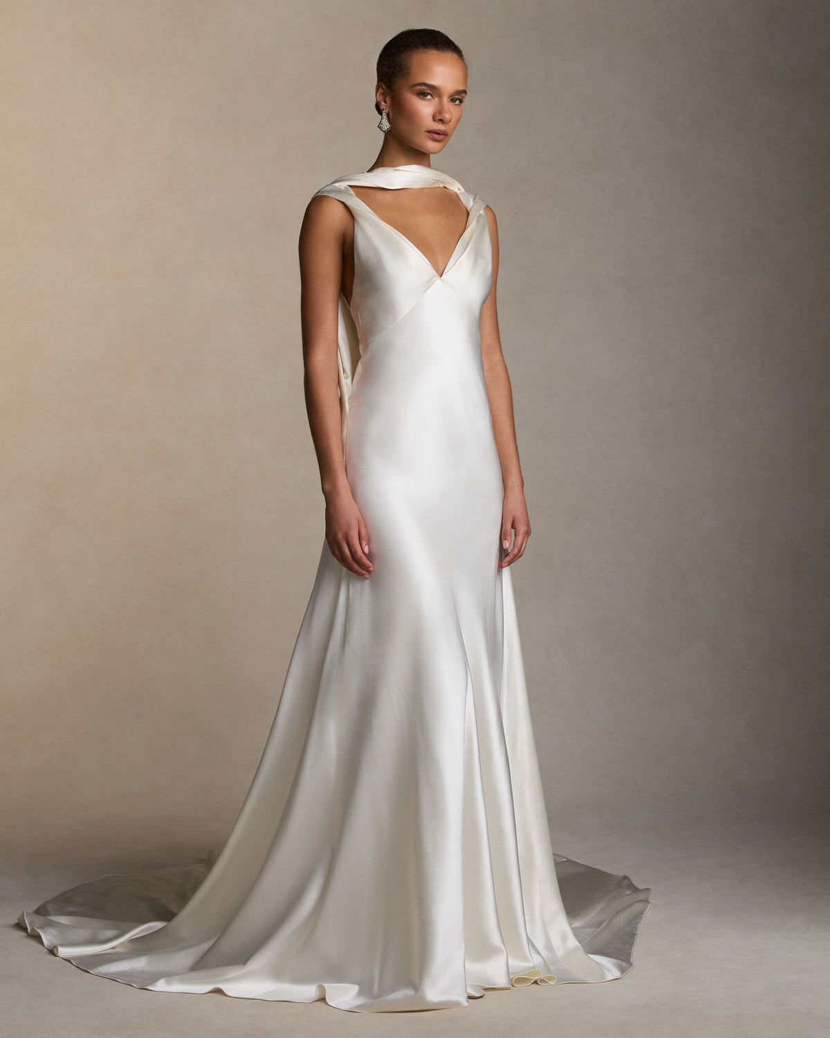 Silk wool bias cut V neck gown. Straps peel away at shoulders, intertwining with a neck drape that falls into an open deep V at back. Diagonal seam detail at center back skirt releases into full train. Invisible zip closure at center back. 