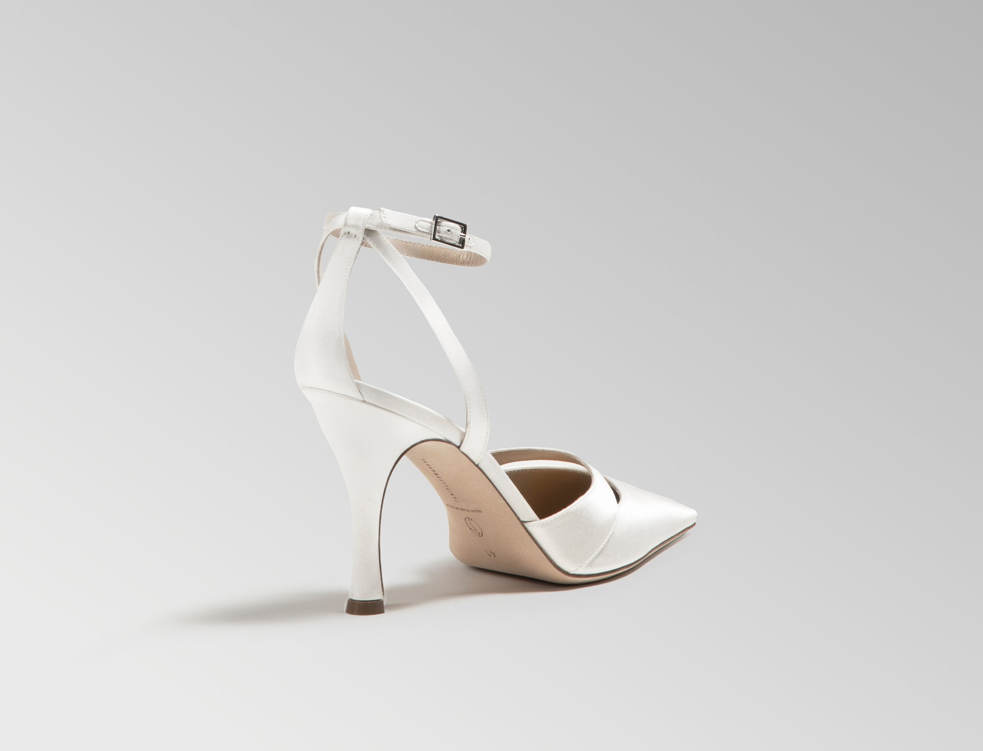 Ivory satin square toe pump with cutout detail at toes. Straps loop around ankle finishing in a buckle closure. 100mm heel. Hand crafted in Italy.