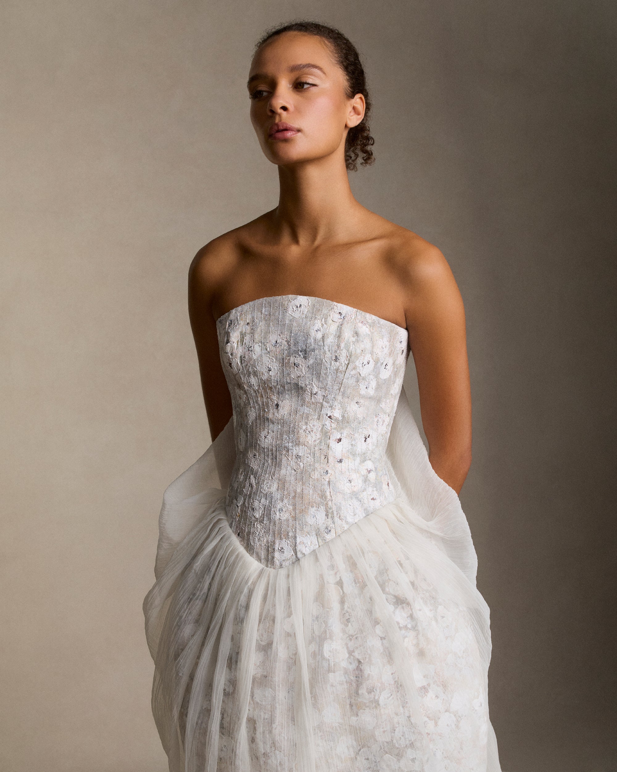 Floral hand painted strapless gown with structured silk wool trapunto stitched bodice and transparent crinkle organza tulip skirt overlay. Skirt drapes into a watteau at center back and falls into an exaggerated train. Boned internal bustier, internal grosgrain belt and invisible zip closure at center back. 