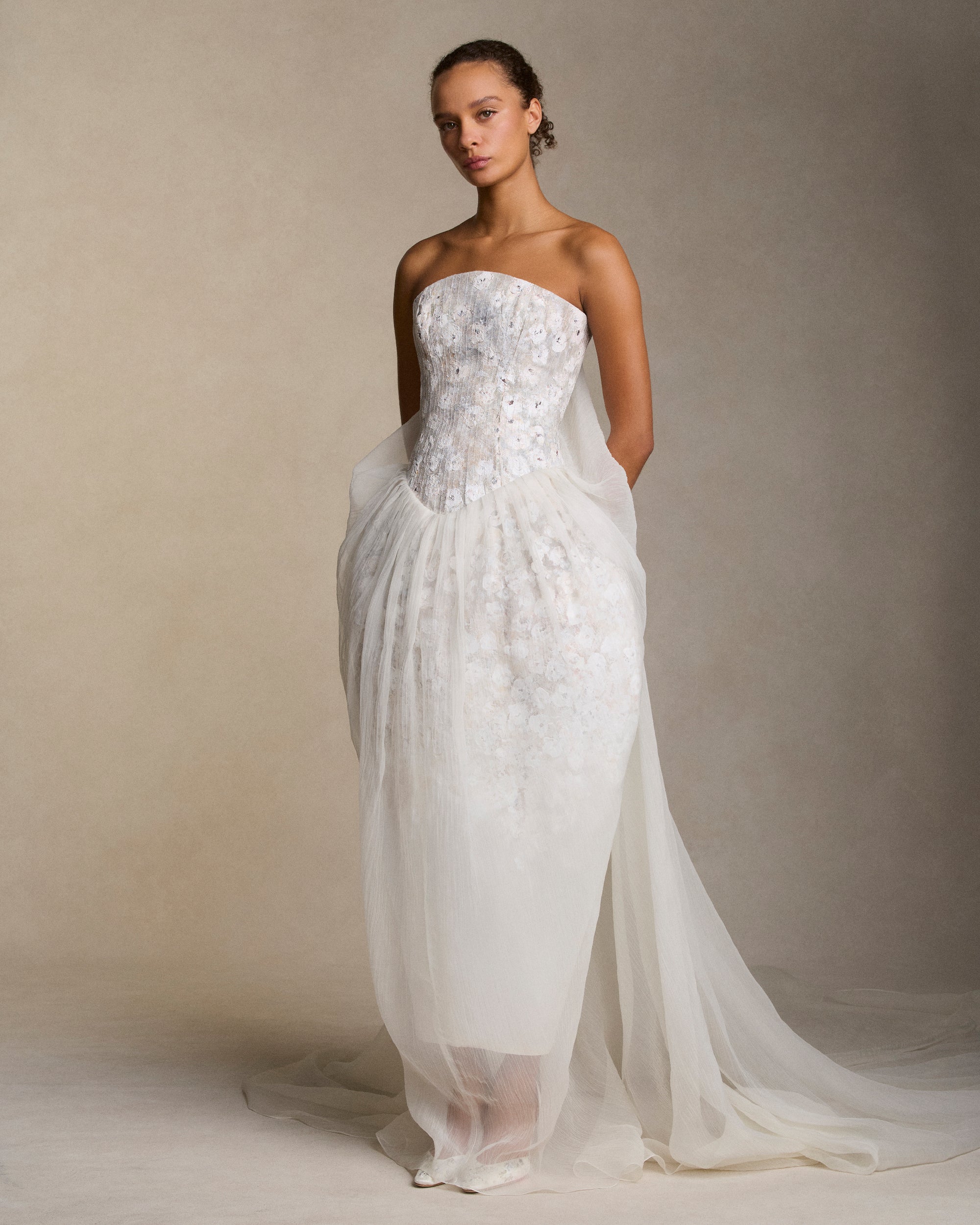 Floral hand painted strapless gown with structured silk wool trapunto stitched bodice and transparent crinkle organza tulip skirt overlay. Skirt drapes into a watteau at center back and falls into an exaggerated train. Boned internal bustier, internal grosgrain belt and invisible zip closure at center back. 