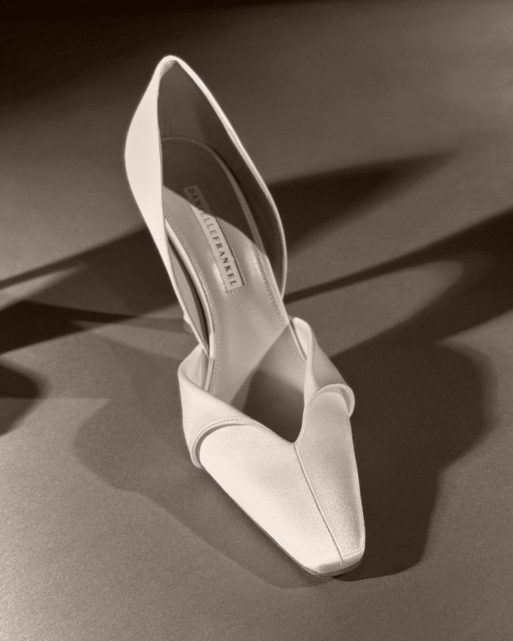 Rounded square toe pump crafted in Italy of ivory satin. Sculpted satin detail peels away at neckline as it wraps around the foot. 100mm heel.