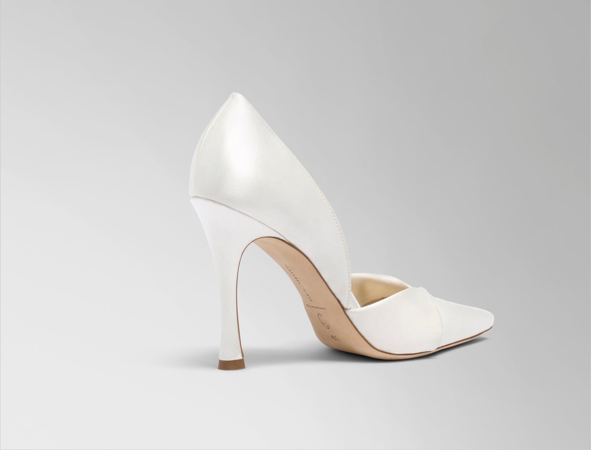 Rounded square toe pump crafted in Italy of ivory satin. Sculpted satin detail peels away at neckline as it wraps around the foot. 100mm heel.