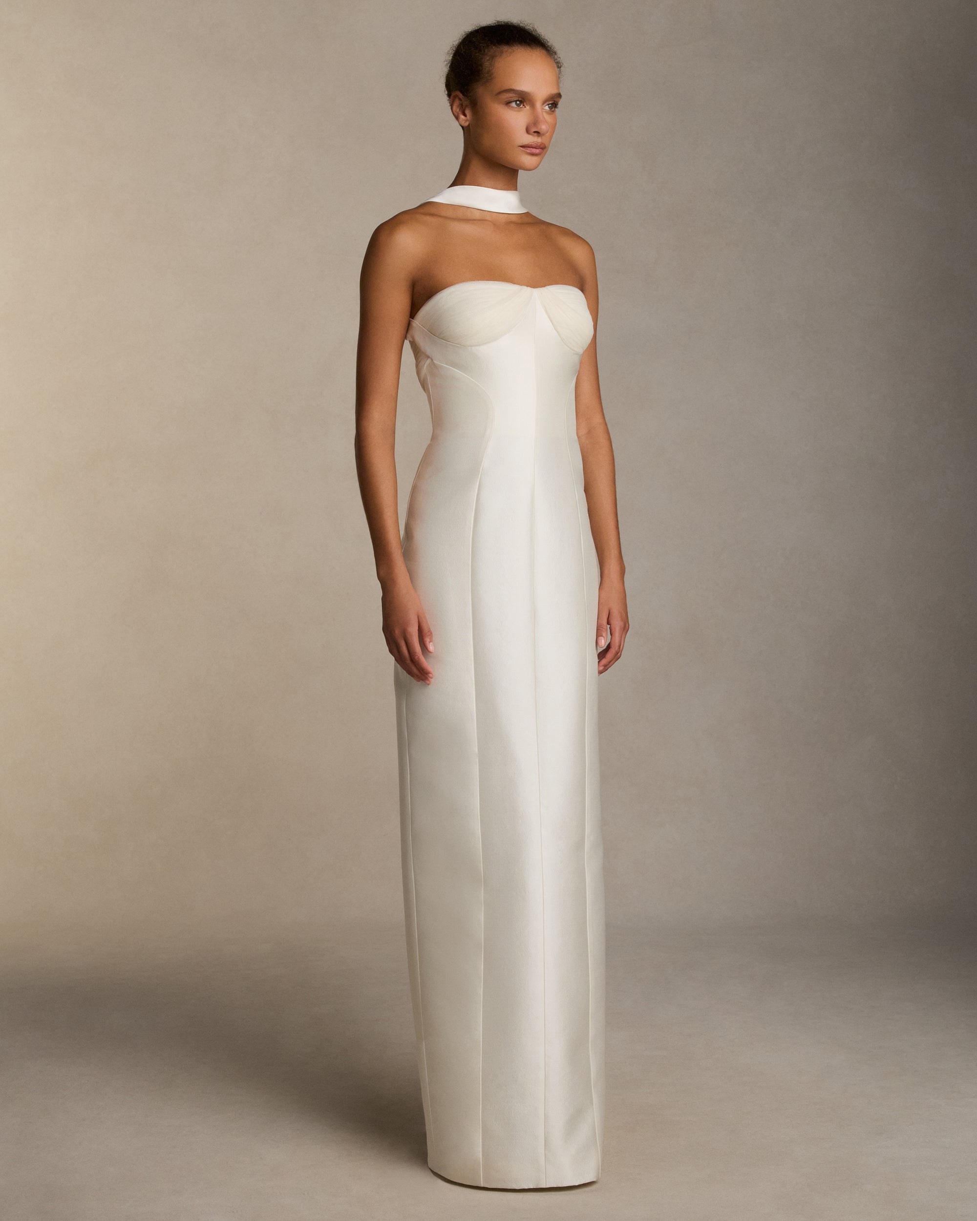 Silk wool twill column gown with curved shaped seams and attached neck wrap detail. Gathered and draped tulle frames the bust wrapping towards the center back. Boned internal bustier, internal grosgrain belt and invisible zip closure at center back.