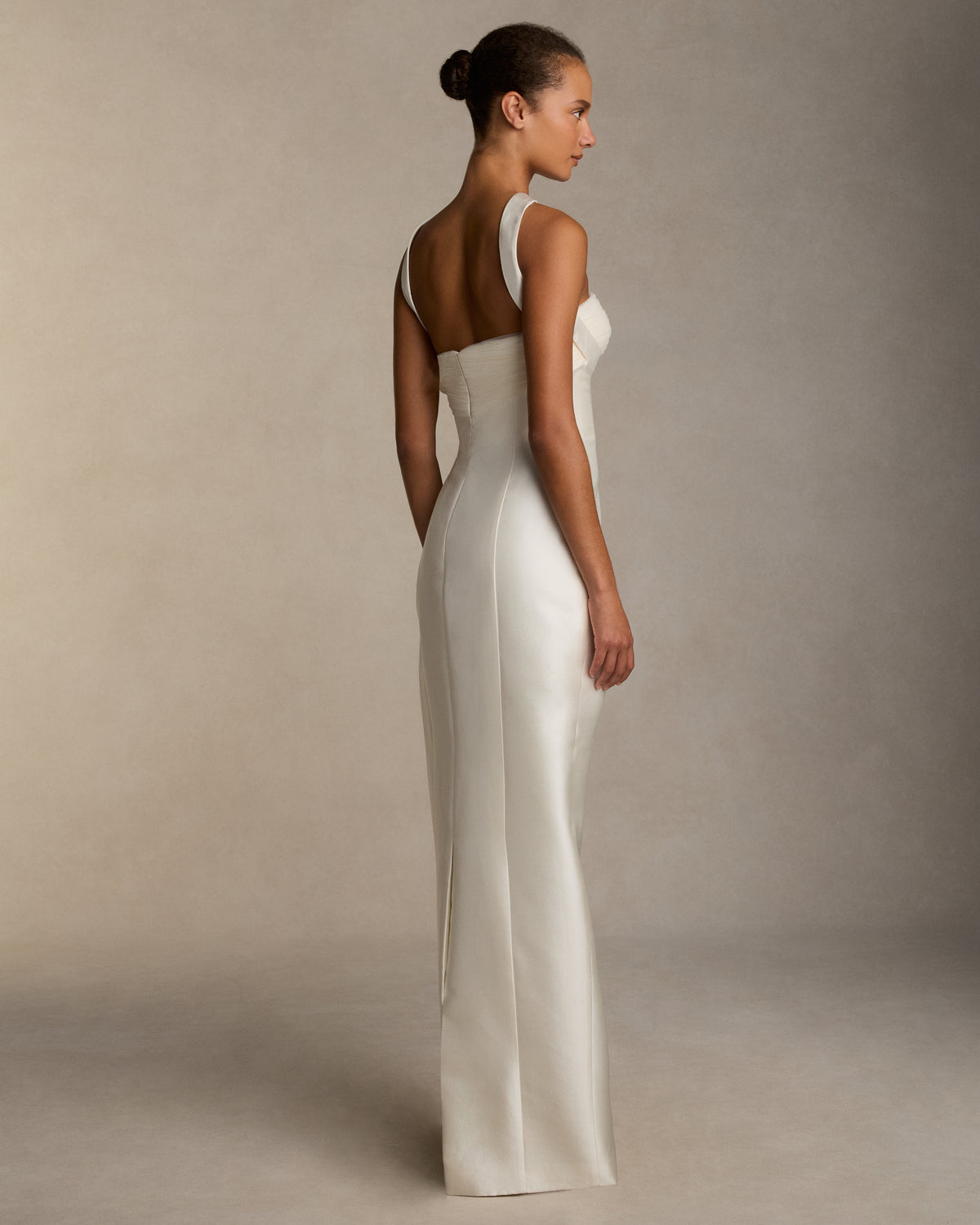 Silk wool twill column gown with curved shaped seams and attached neck wrap detail. Gathered and draped tulle frames the bust wrapping towards the center back. Boned internal bustier, internal grosgrain belt and invisible zip closure at center back.