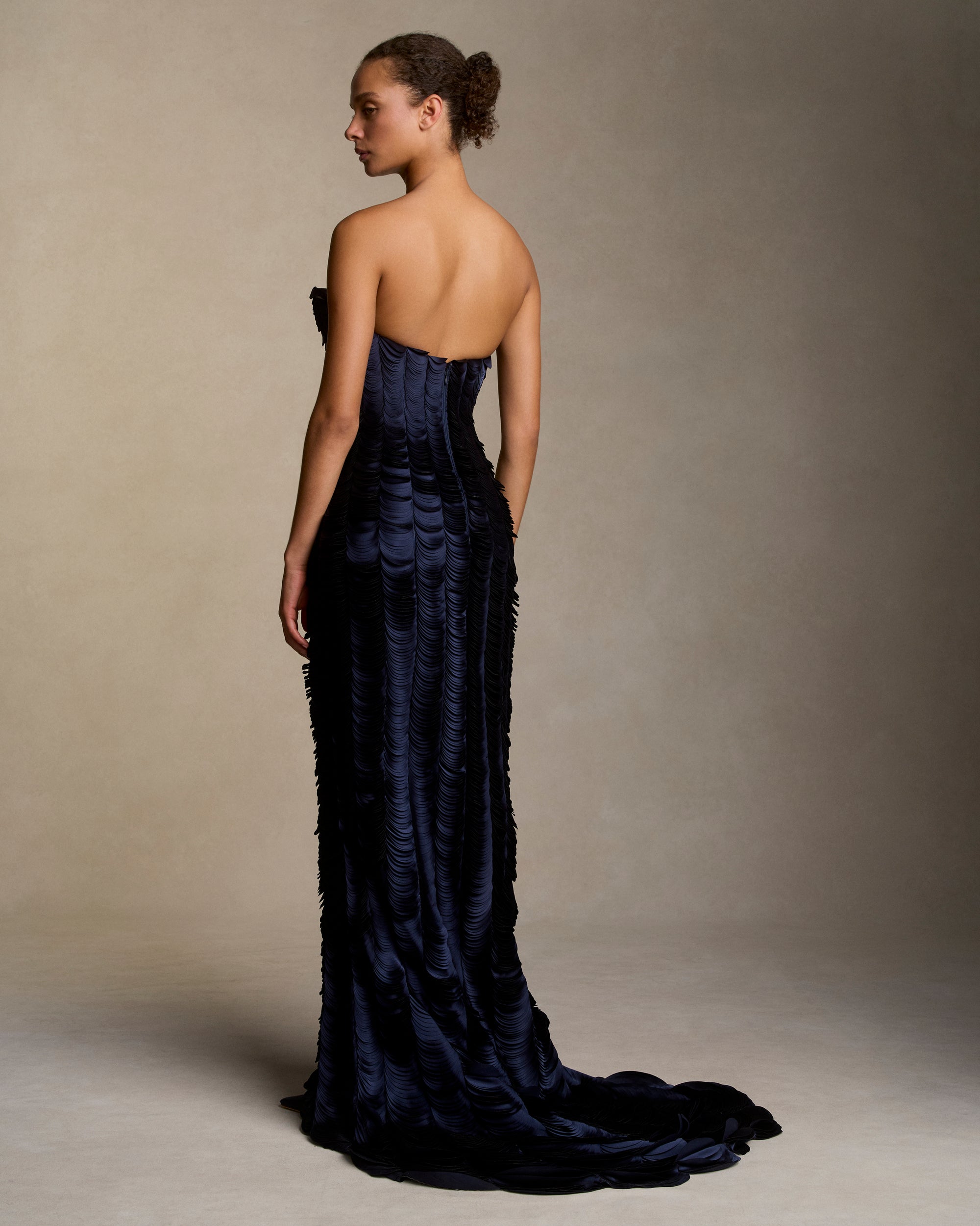 Strapless satin gown with flared neckline. Thousands of hand applied lasercut satin petals cascade down the body accentuating the silhouette. Boned internal bustier, internal grosgrain belt and invisible zip closure at center back.
