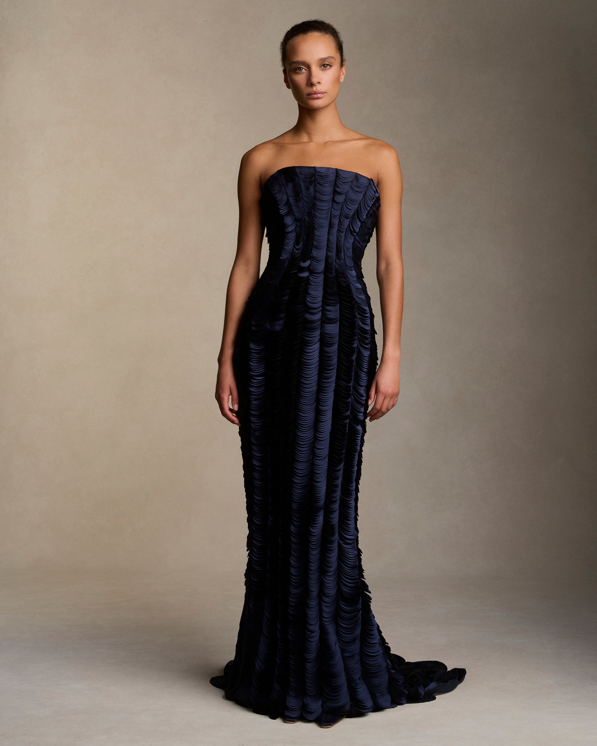 Strapless satin gown with flared neckline. Thousands of hand applied lasercut satin petals cascade down the body accentuating the silhouette. Boned internal bustier, internal grosgrain belt and invisible zip closure at center back.