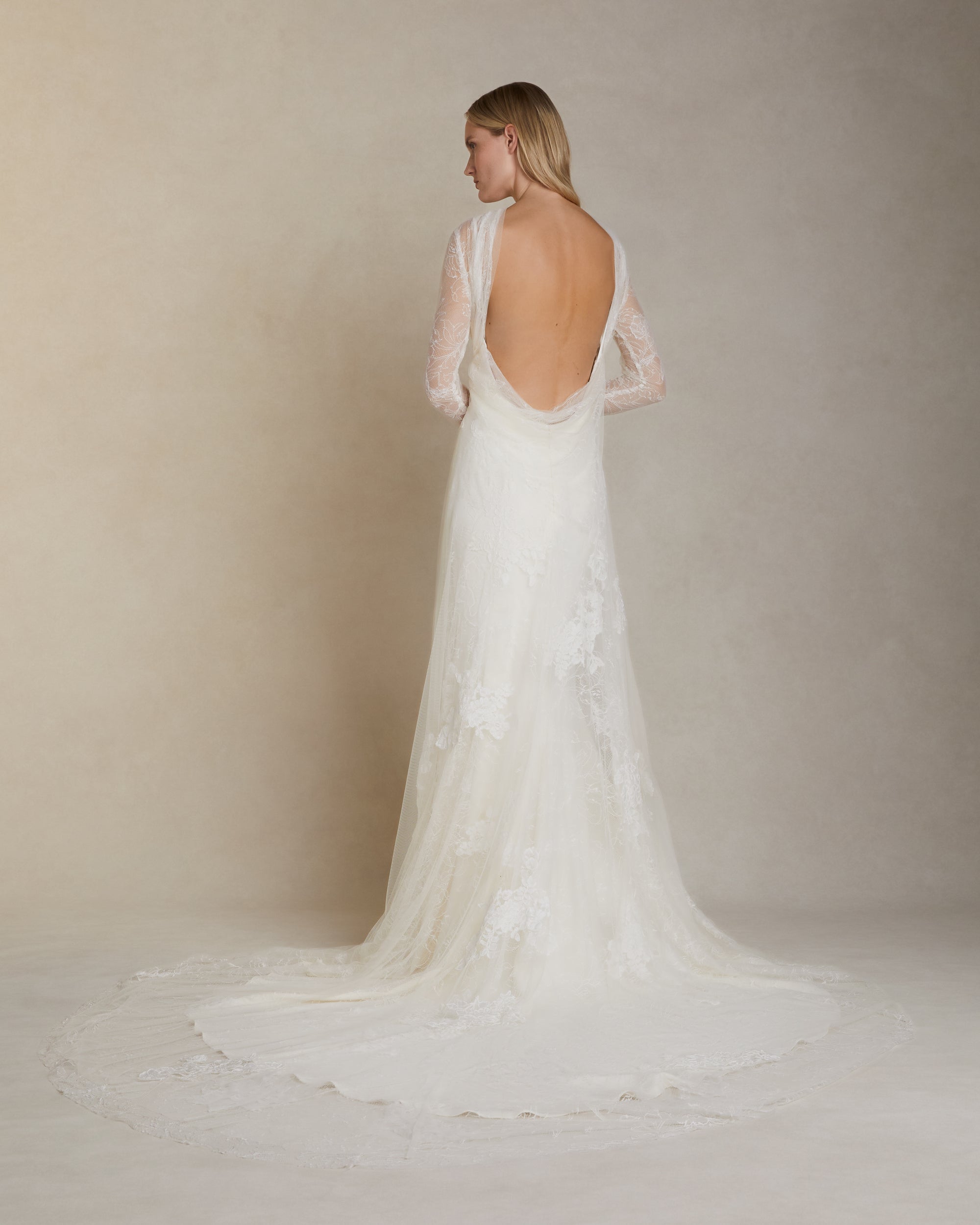 Romantic long sleeve iris lace and soft tulle gown adorned with hand cut chantilly and corded lace appliqués. A diaphanous overlay extends beyond a stretch Cady spaghetti strap foundation into delicate draping across neck and decolletage, spilling into a scarf drape detail at low back. Boned internal bustier, internal grosgrain waist belt and center back zip closure.