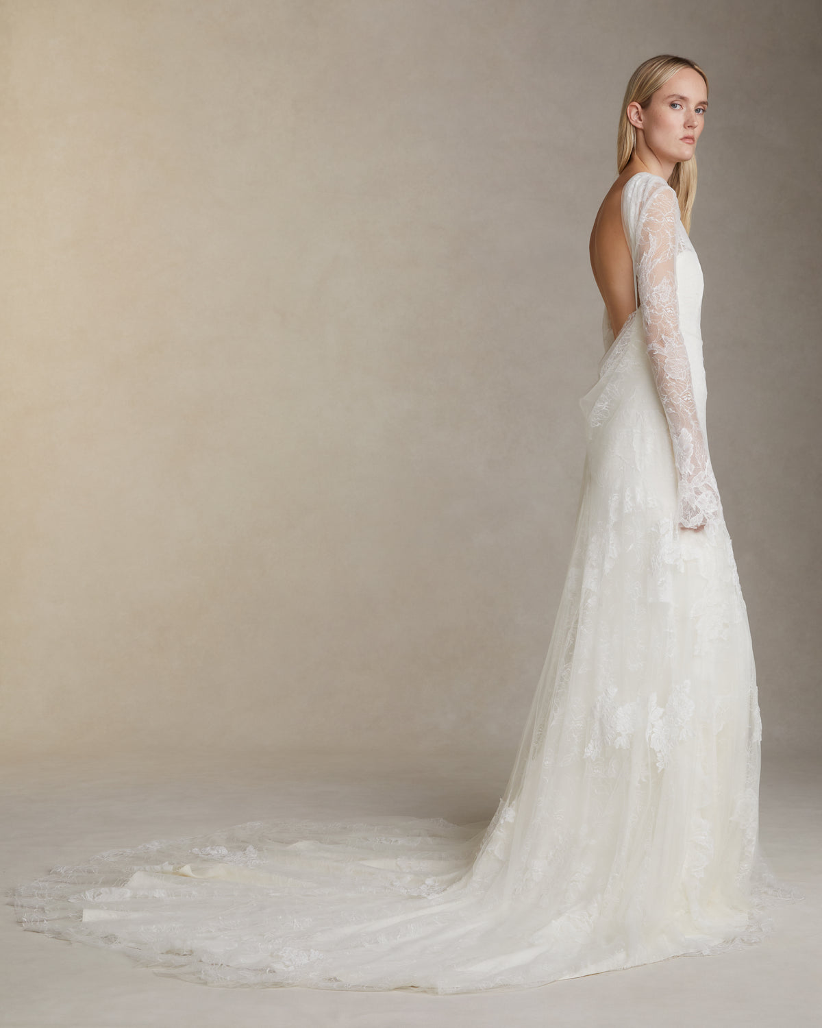 Romantic long sleeve iris lace and soft tulle gown adorned with hand cut chantilly and corded lace appliqués. A diaphanous overlay extends beyond a stretch Cady spaghetti strap foundation into delicate draping across neck and decolletage, spilling into a scarf drape detail at low back. Boned internal bustier, internal grosgrain waist belt and center back zip closure.