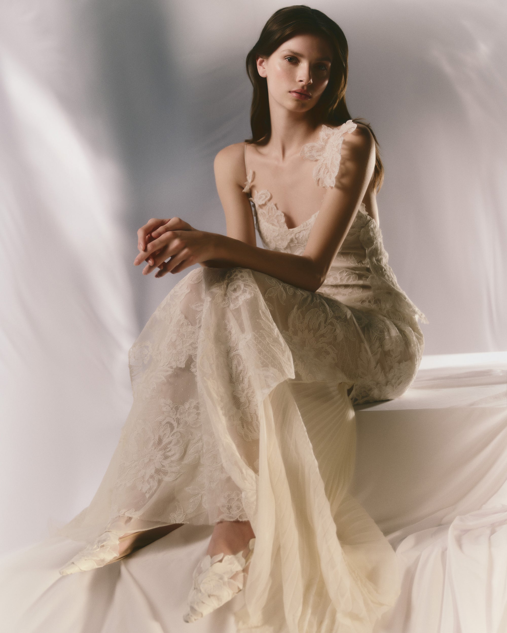 Lyon lace gown with pleated chiffon godets and hand cut Lyon lace applique throughout. Hand cut lace adorns the spaghetti straps and watteau peels from center back releasing into an extended pleated chiffon train. Soft internal bustier. Invisible zip closure at center back.