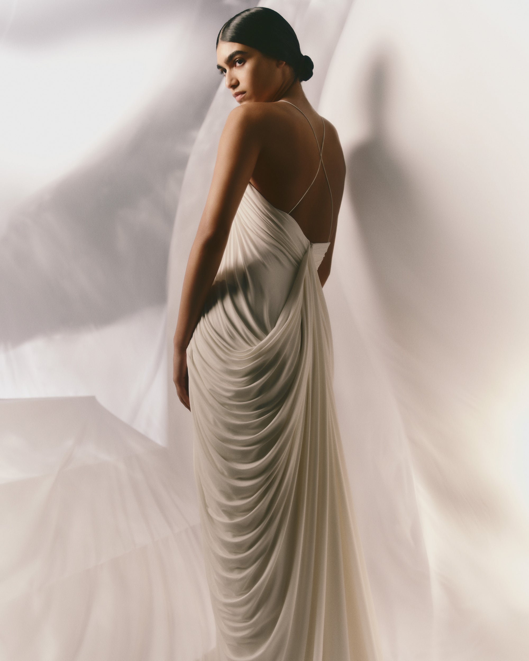 Fluid jersey gown with dramatic scooped neckline and cross back spaghetti straps. Watteau detail cascades from the center back into a puddle train. Invisible zip closure at center back.