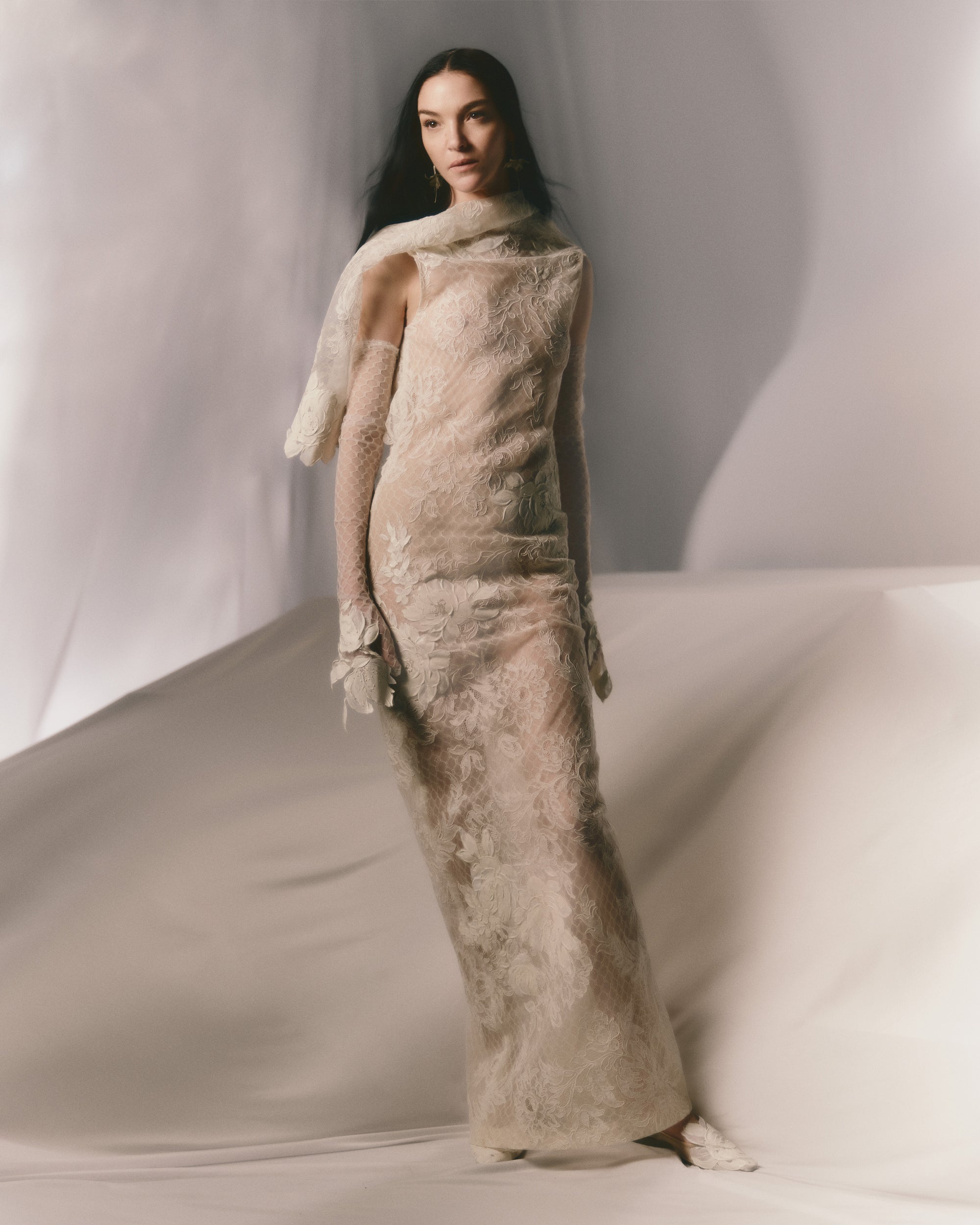 Lyon lace gown framed in silk honeycomb netting and decorated with handpainted florals throughout. Asymmetric cowl neckline falls into a peeled away back. Nude charmeuse lining. Invisible zip closure at center back.