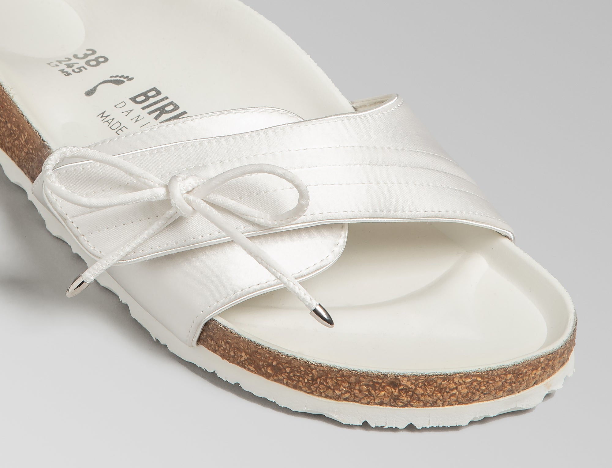 BIRKENSTOCK’s original 1963 design is reimagined by Danielle Frankel in a pure, minimalist silhouette with a delicate satin upper. A satin cord with metal-tipped ends adds refined elegance. The design also introduces an innovative adjustable hidden buckle closure, while handcrafted German craftsmanship ensures the iconic comfort and quality BIRKENSTOCK is known for. - Upper: Delicate satin upper, bow detail with metal ends- Footbed: Anatomical shaped BIRKENSTOCK cork latex Footbed lined with premium Nappa Leather- Sole: EVA die cut outsole with a custom design, blending classic BIRKENSTOCK bone pattern with delicate leaf inspired detailing