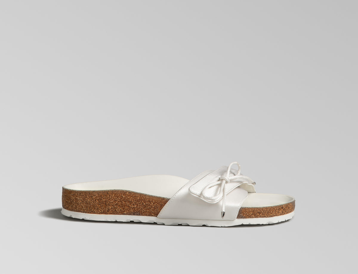 BIRKENSTOCK’s original 1963 design is reimagined by Danielle Frankel in a pure, minimalist silhouette with a delicate satin upper. A satin cord with metal-tipped ends adds refined elegance. The design also introduces an innovative adjustable hidden buckle closure, while handcrafted German craftsmanship ensures the iconic comfort and quality BIRKENSTOCK is known for. - Upper: Delicate satin upper, bow detail with metal ends- Footbed: Anatomical shaped BIRKENSTOCK cork latex Footbed lined with premium Nappa Leather- Sole: EVA die cut outsole with a custom design, blending classic BIRKENSTOCK bone pattern with delicate leaf inspired detailing