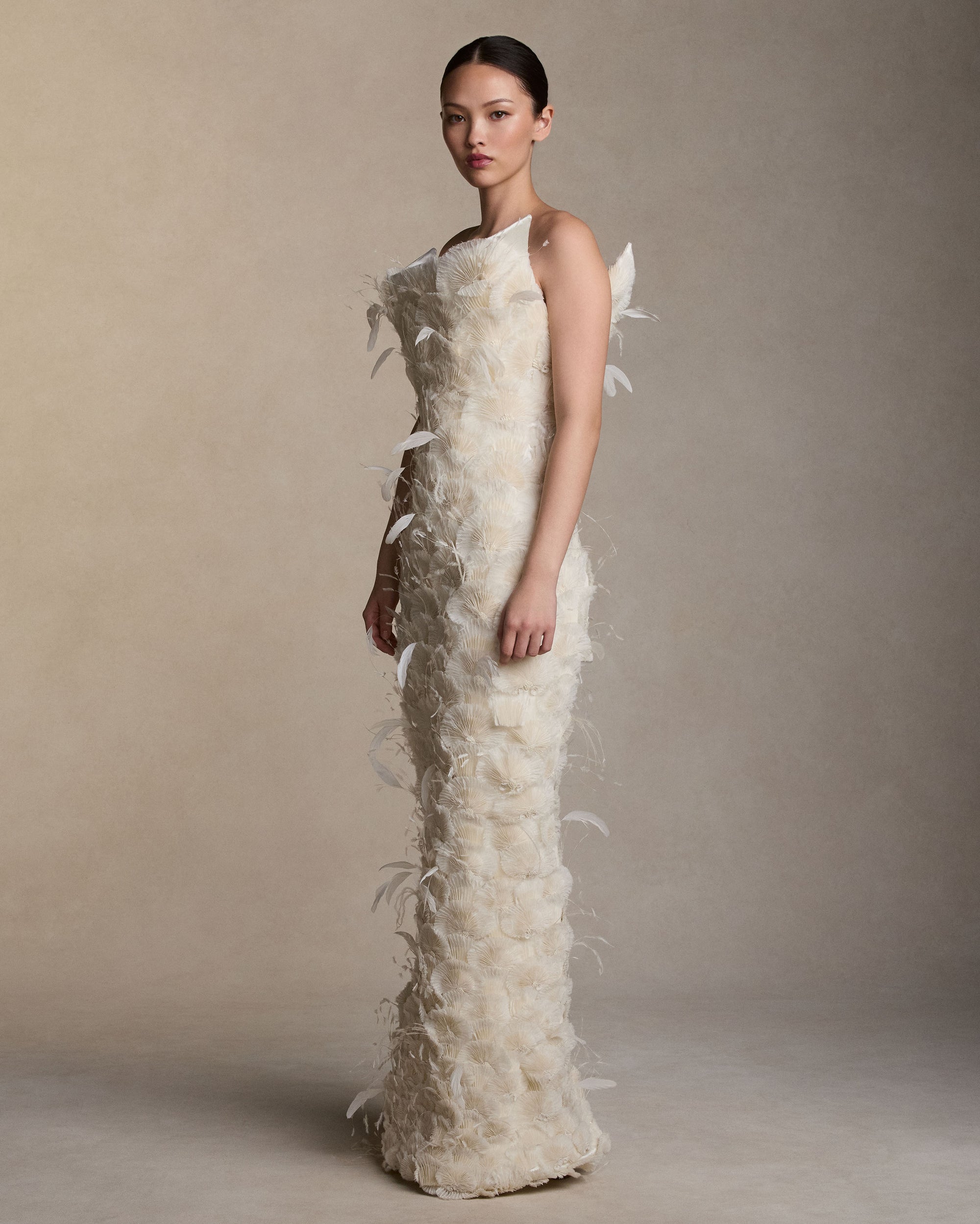 Silk and feather embroidered strapless column gown with exaggerated flared neckline. Stripped crinkle organza and satin organza create a fan motif embroidery tipped in delicate threadwork and feather plumes. Boned internal double zip bustier with internal grosgrain belt. 