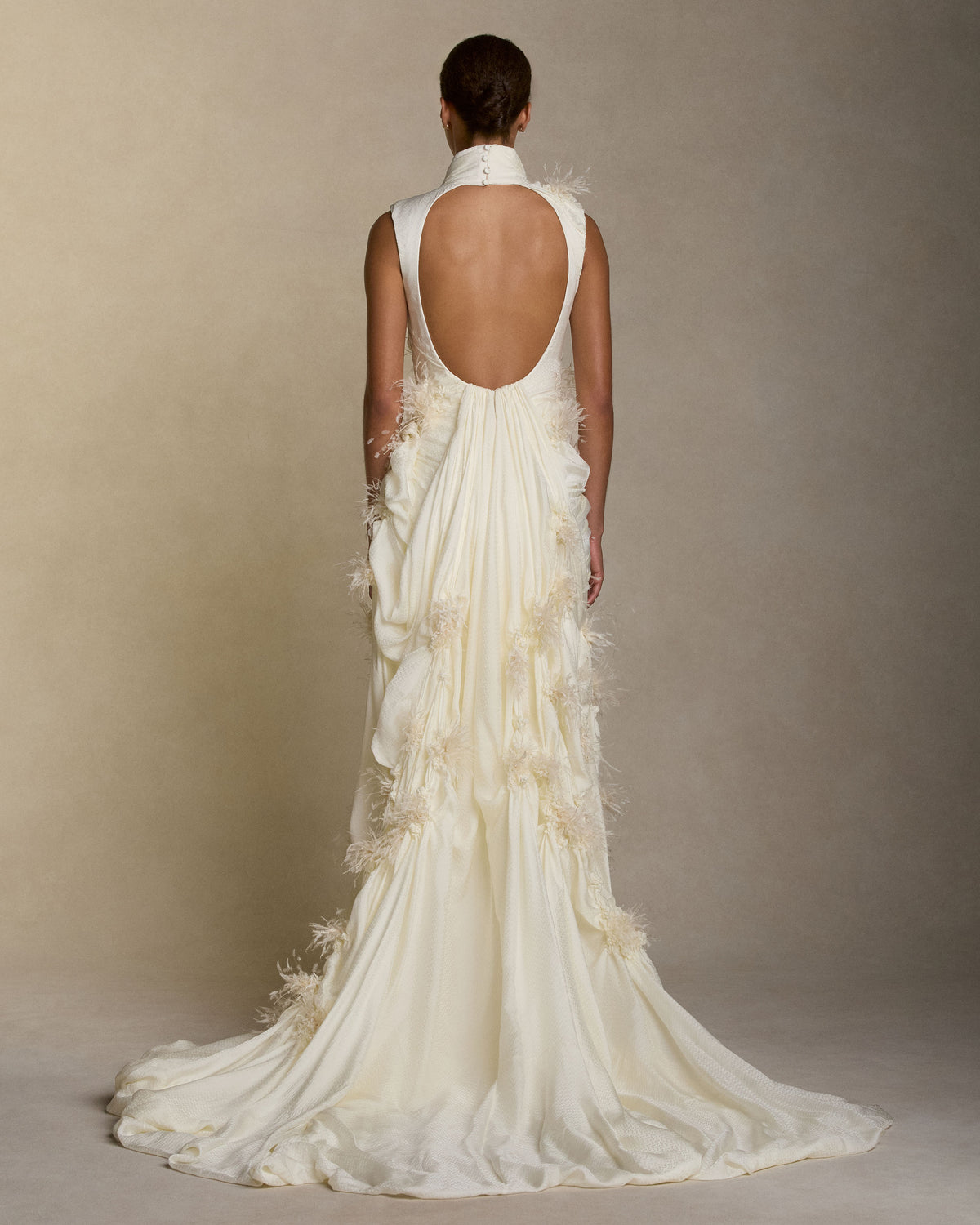 Habotai À pois high-neck gown with an open back detail. Asymmetric, fluid swagged draping shapes the silhouette, with scattered smocked floral embroidery accented by feather and crinkle organza detailing. Soft internal bustier; self fabric covered button closure sleeve opening and back neck, invisible zip at waist.
