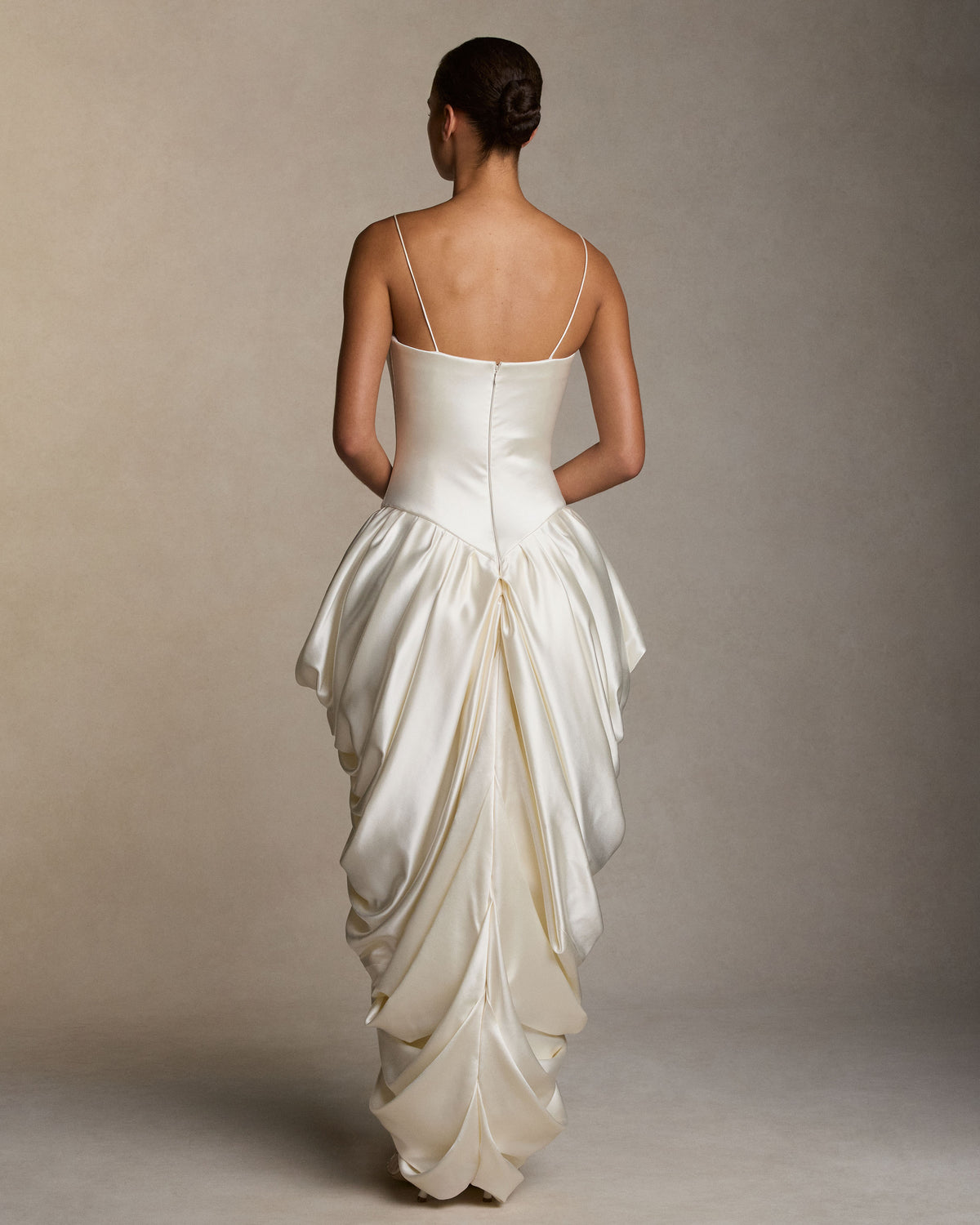 Silk wool spaghetti strap gown with elongated bodice, cascading draping falls from the waist creating a tulip skirt silhouette. Internal grosgrain waist belt, invisible zip at center back. Styled with Kate jacket