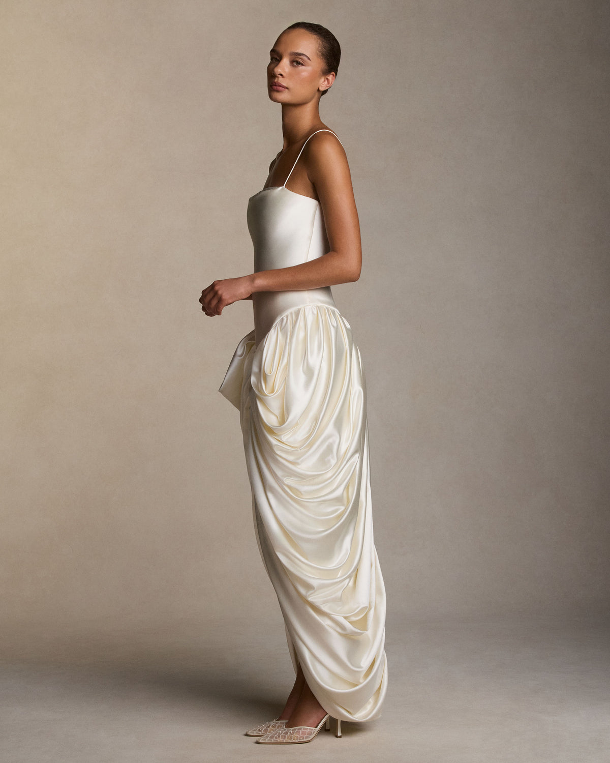 Silk wool spaghetti strap gown with elongated bodice, cascading draping falls from the waist creating a tulip skirt silhouette. Internal grosgrain waist belt, invisible zip at center back. Styled with Kate jacket