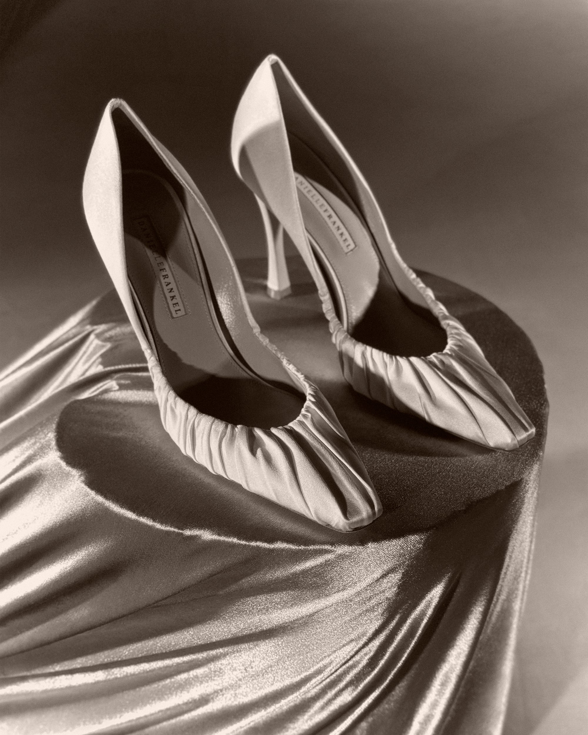 Rounded square toe pump crafted in Italy of ivory satin. Gathered satin draping at toe fades into smooth satin finish at back. 100mm heel.