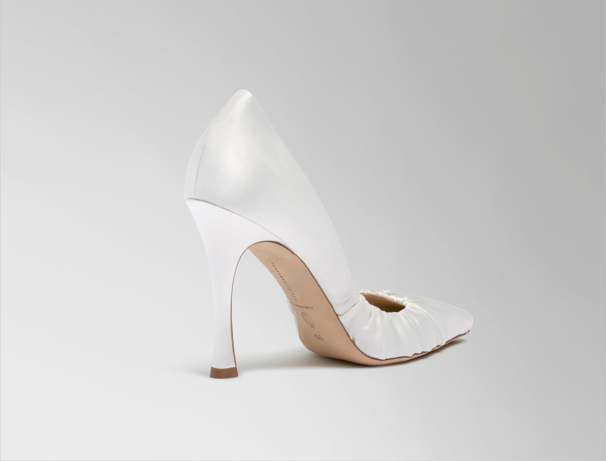 Rounded square toe pump crafted in Italy of ivory satin. Gathered satin draping at toe fades into smooth satin finish at back. 100mm heel.