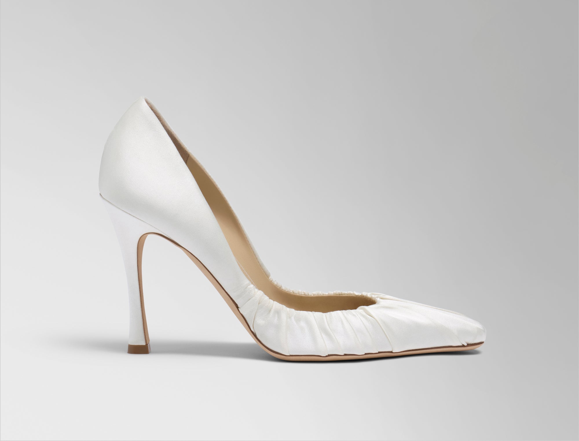 Rounded square toe pump crafted in Italy of ivory satin. Gathered satin draping at toe fades into smooth satin finish at back. 100mm heel.