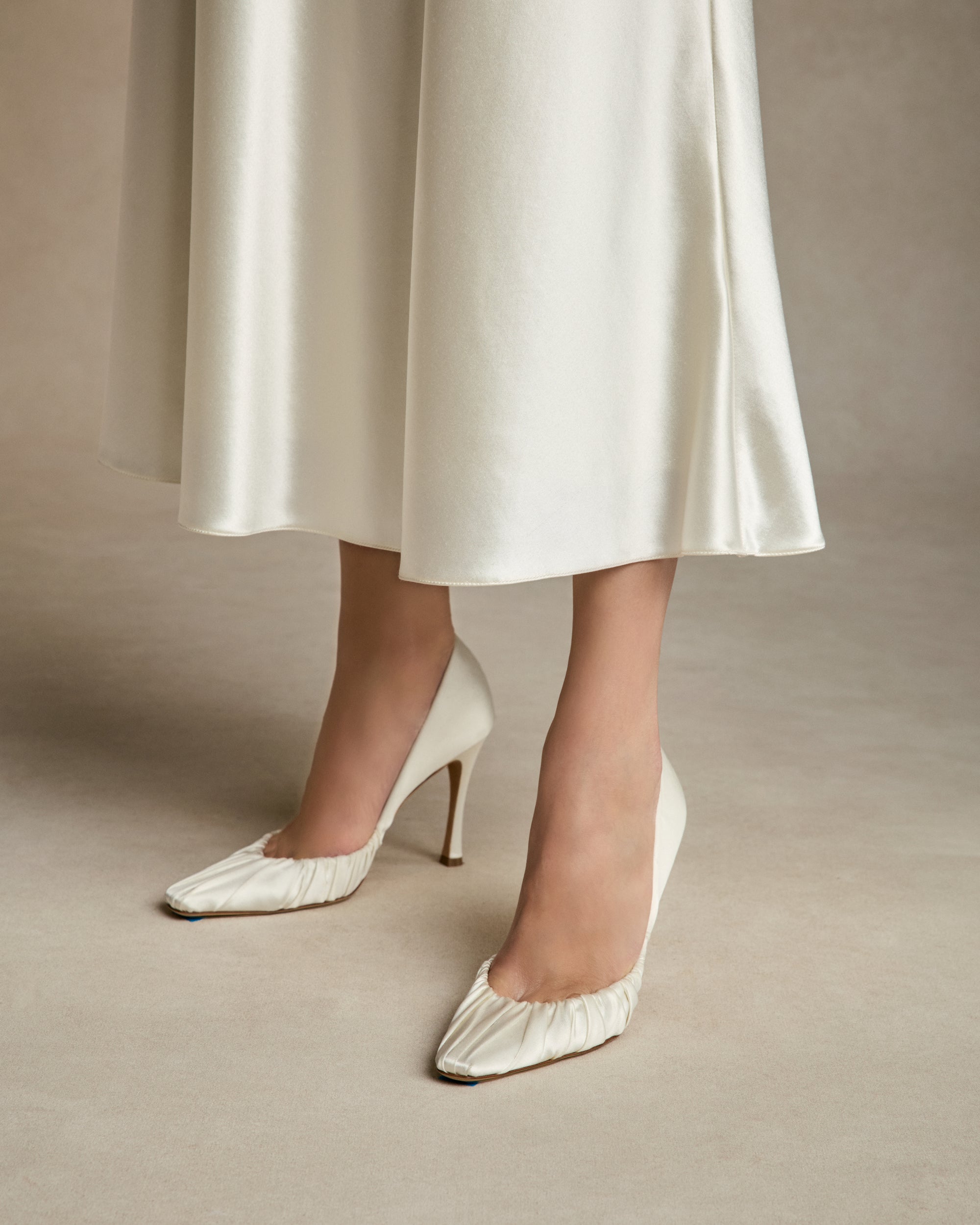 Rounded square toe pump crafted in Italy of ivory satin. Gathered satin draping at toe fades into smooth satin finish at back. 100mm heel.