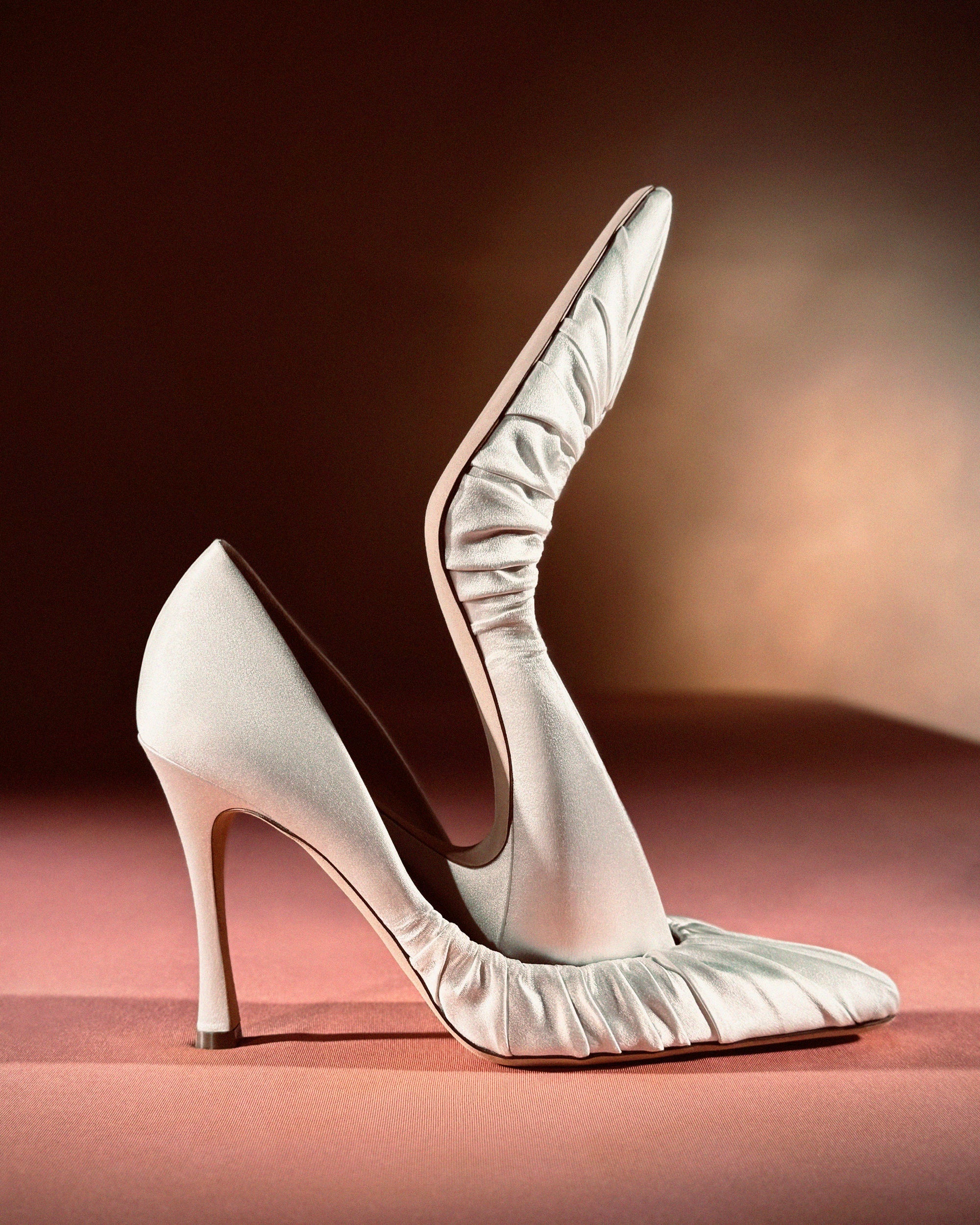Rounded square toe pump crafted in Italy of ivory satin. Gathered satin draping at toe fades into smooth satin finish at back. 100mm heel.