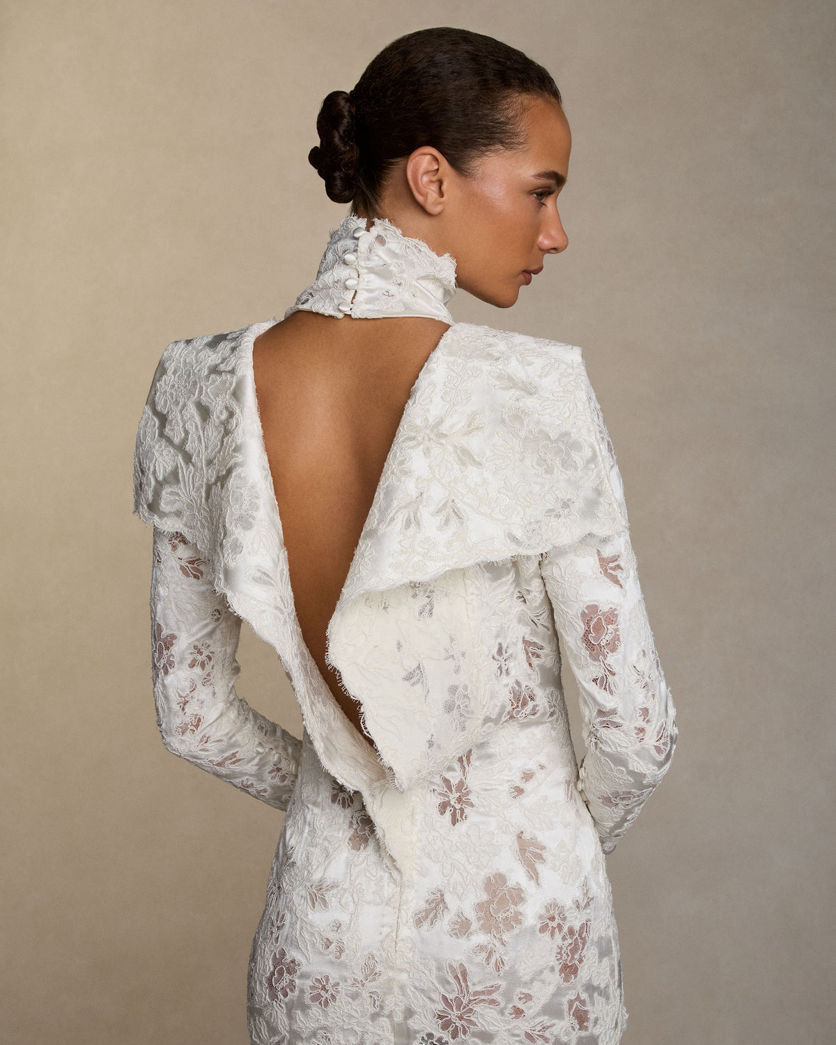 Silk wool gown with corded lace and a sculptural, peeling open back detail. Lustrous silk wool is layered with corded lace, re-embroidered and delicately cut away to create dimensional layers of transparency and shine. Self fabric covered buttons at wrist, invisible zip closure at center back. 