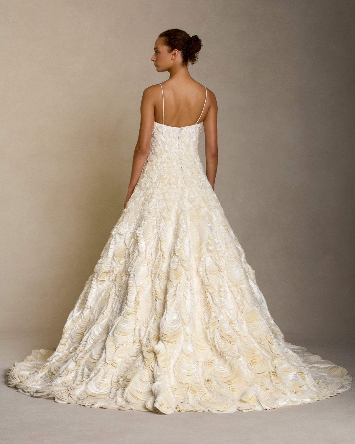 Dipped neckline spaghetti strap ballgown decorated entirely with hand cut silk wool cascading petal embroidery. Thousands of hand applied silk wool petals undulate with texture throughout the gown falling into a dramatic bubble hem. Boned internal bustier, internal grosgrain belt and invisible zip closure at center back.