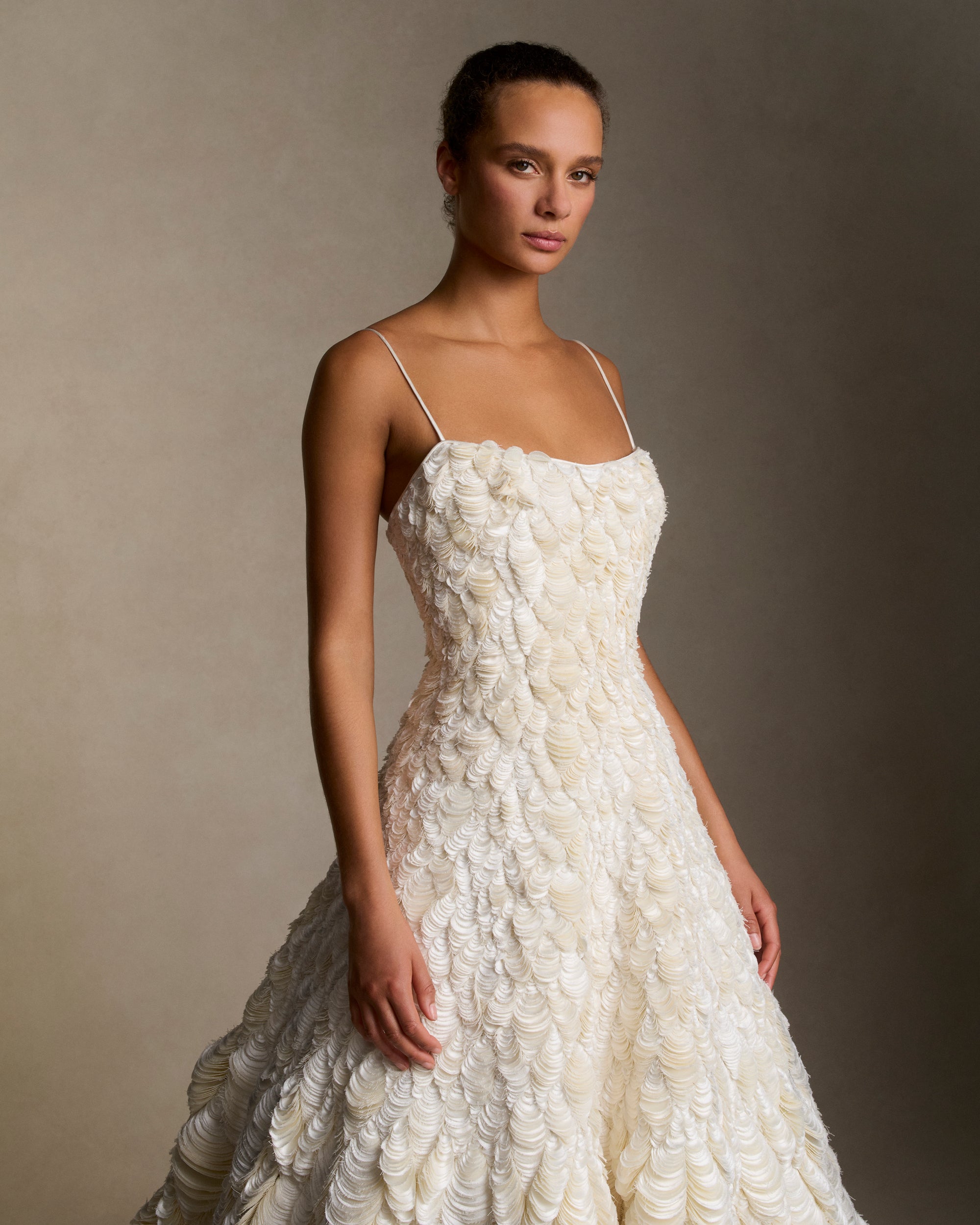 Dipped neckline spaghetti strap ballgown decorated entirely with hand cut silk wool cascading petal embroidery. Thousands of hand applied silk wool petals undulate with texture throughout the gown falling into a dramatic bubble hem. Boned internal bustier, internal grosgrain belt and invisible zip closure at center back.