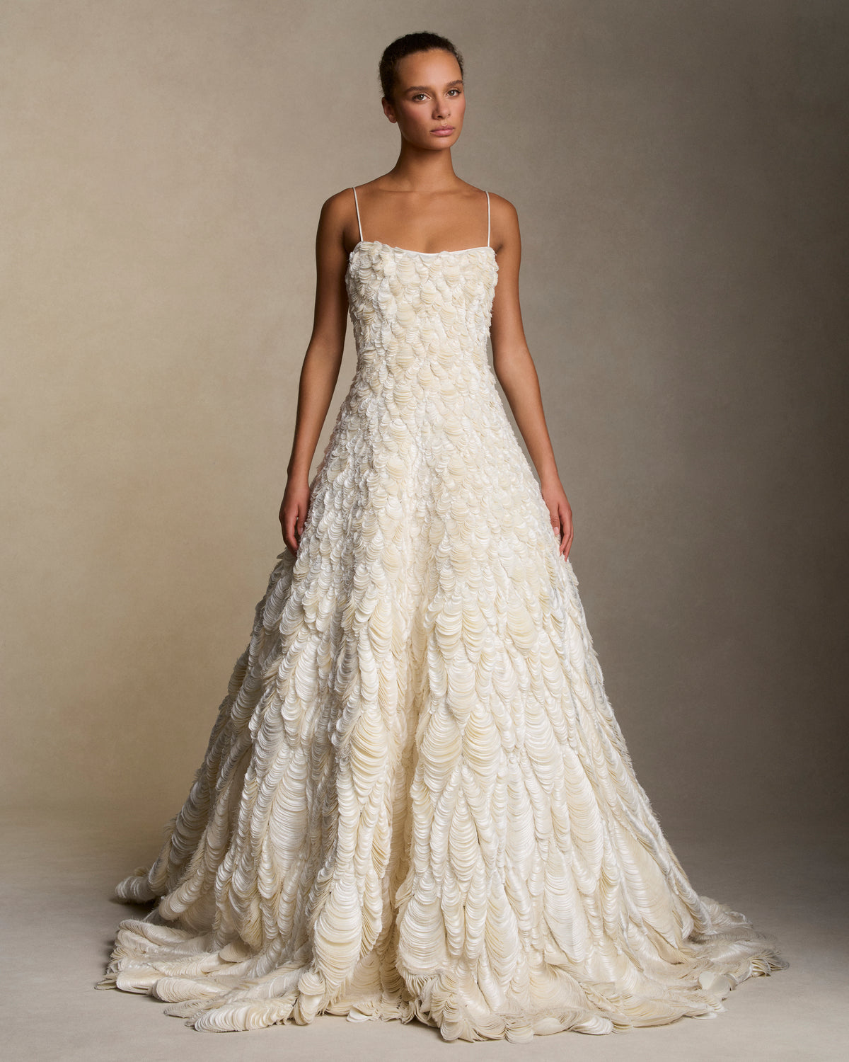 Dipped neckline spaghetti strap ballgown decorated entirely with hand cut silk wool cascading petal embroidery. Thousands of hand applied silk wool petals undulate with texture throughout the gown falling into a dramatic bubble hem. Boned internal bustier, internal grosgrain belt and invisible zip closure at center back.