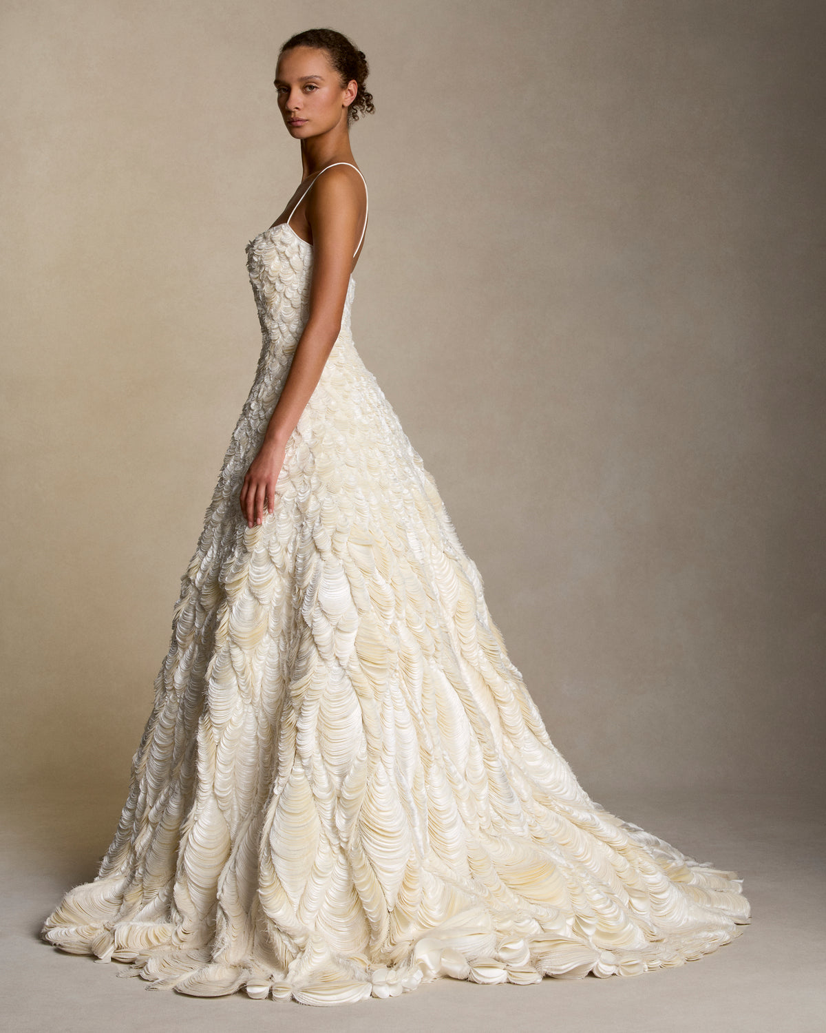 Dipped neckline spaghetti strap ballgown decorated entirely with hand cut silk wool cascading petal embroidery. Thousands of hand applied silk wool petals undulate with texture throughout the gown falling into a dramatic bubble hem. Boned internal bustier, internal grosgrain belt and invisible zip closure at center back.