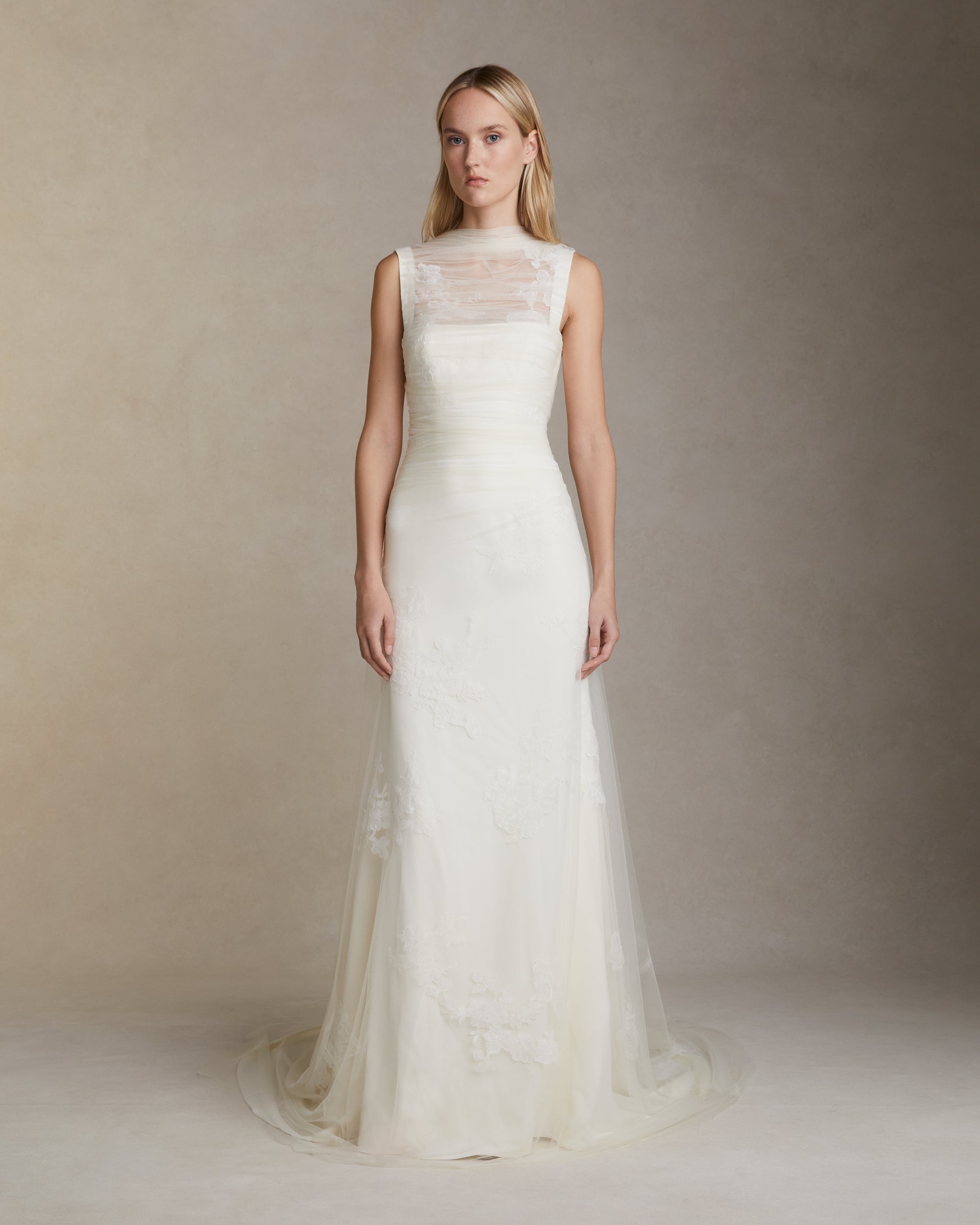Stretch cady gown with draped soft tulle overlay decorated in hand cut corded and chantilly lace applique. Elongated soft tulle pleated panels drape across bodice and tie at back. Invisible zip closure at center back.