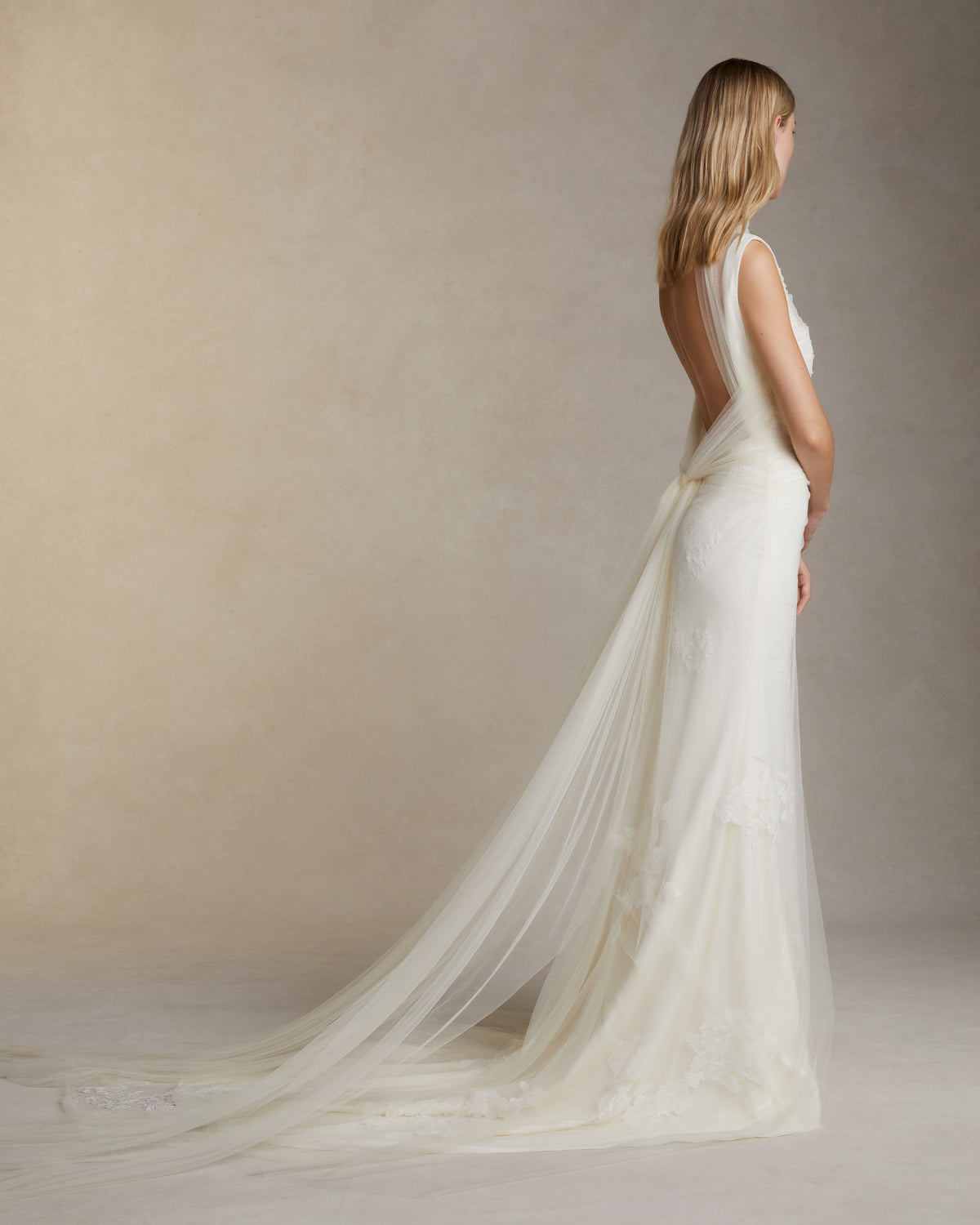 Stretch cady gown with draped soft tulle overlay decorated in hand cut corded and chantilly lace applique. Elongated soft tulle pleated panels drape across bodice and tie at back. Invisible zip closure at center back.