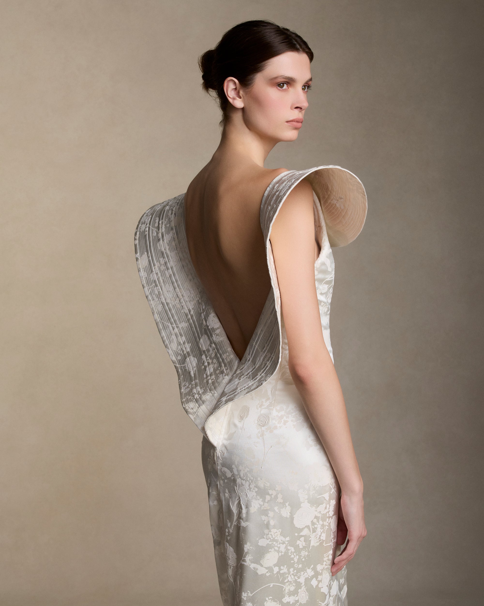 Floral pigment printed and hand painted silk wool column gown. Exaggerated fluted collar drape with trapunto stitch detailing peels from neckline falling down center back. Internal grosgrain belt and invisible zip closure at center back.
