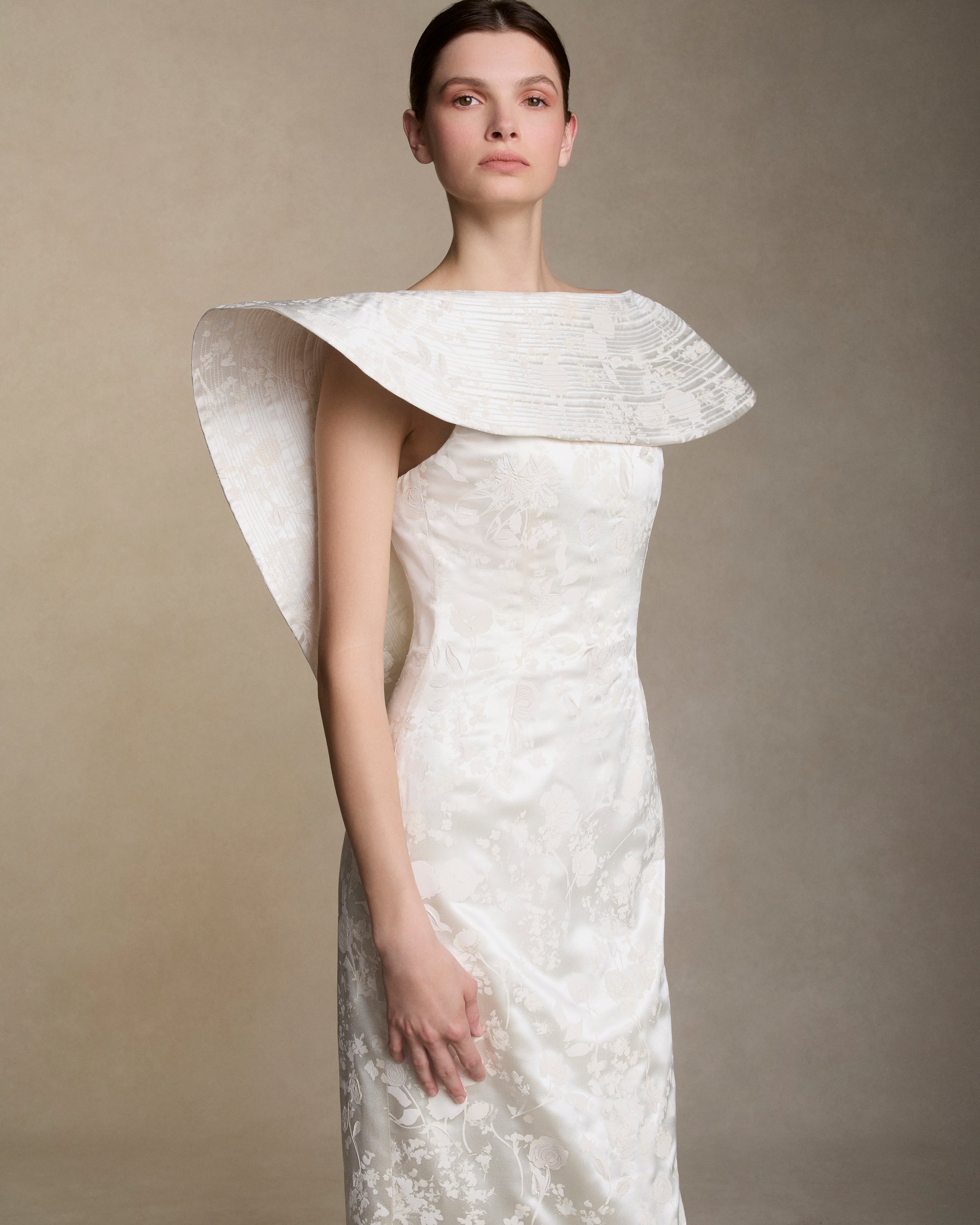 Floral pigment printed and hand painted silk wool column gown. Exaggerated fluted collar drape with trapunto stitch detailing peels from neckline falling down center back. Internal grosgrain belt and invisible zip closure at center back.