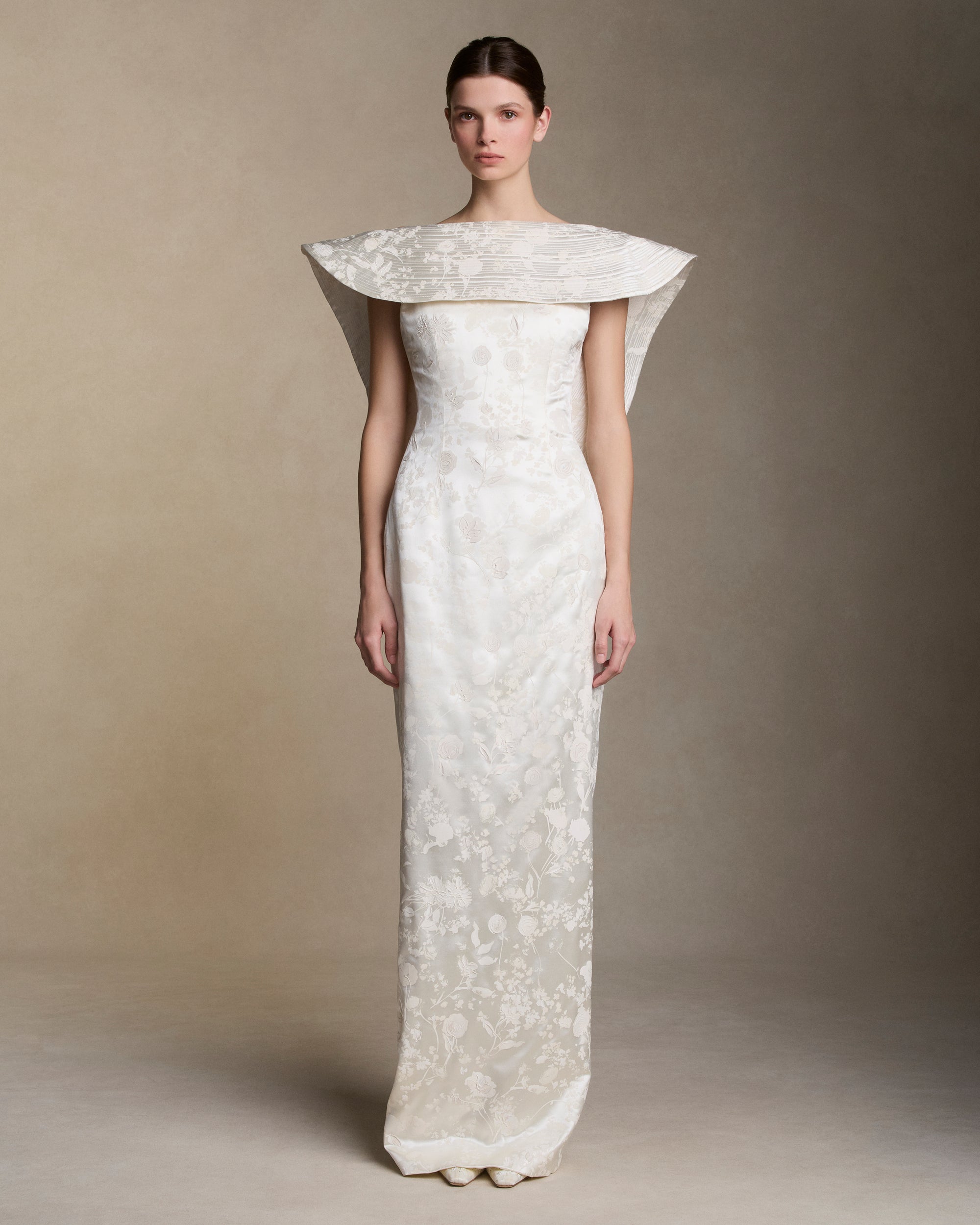 Floral pigment printed and hand painted silk wool column gown. Exaggerated fluted collar drape with trapunto stitch detailing peels from neckline falling down center back. Internal grosgrain belt and invisible zip closure at center back.