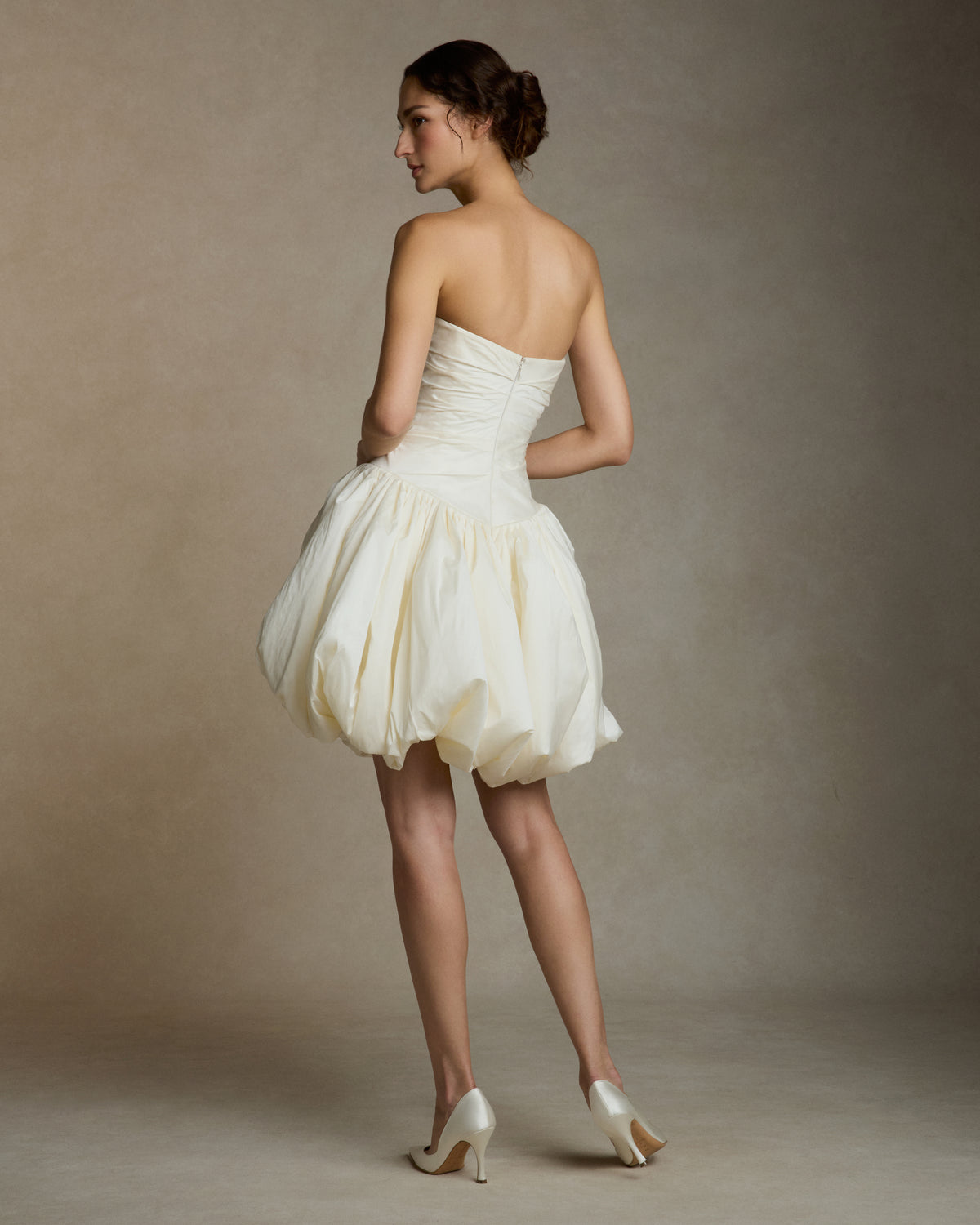 Featherweight silk taffeta draped strapless mini dress with elongated v waistline. Bubble hem skirt releases from the high hip and peels away from the center front. Invisible zip closure at center back.