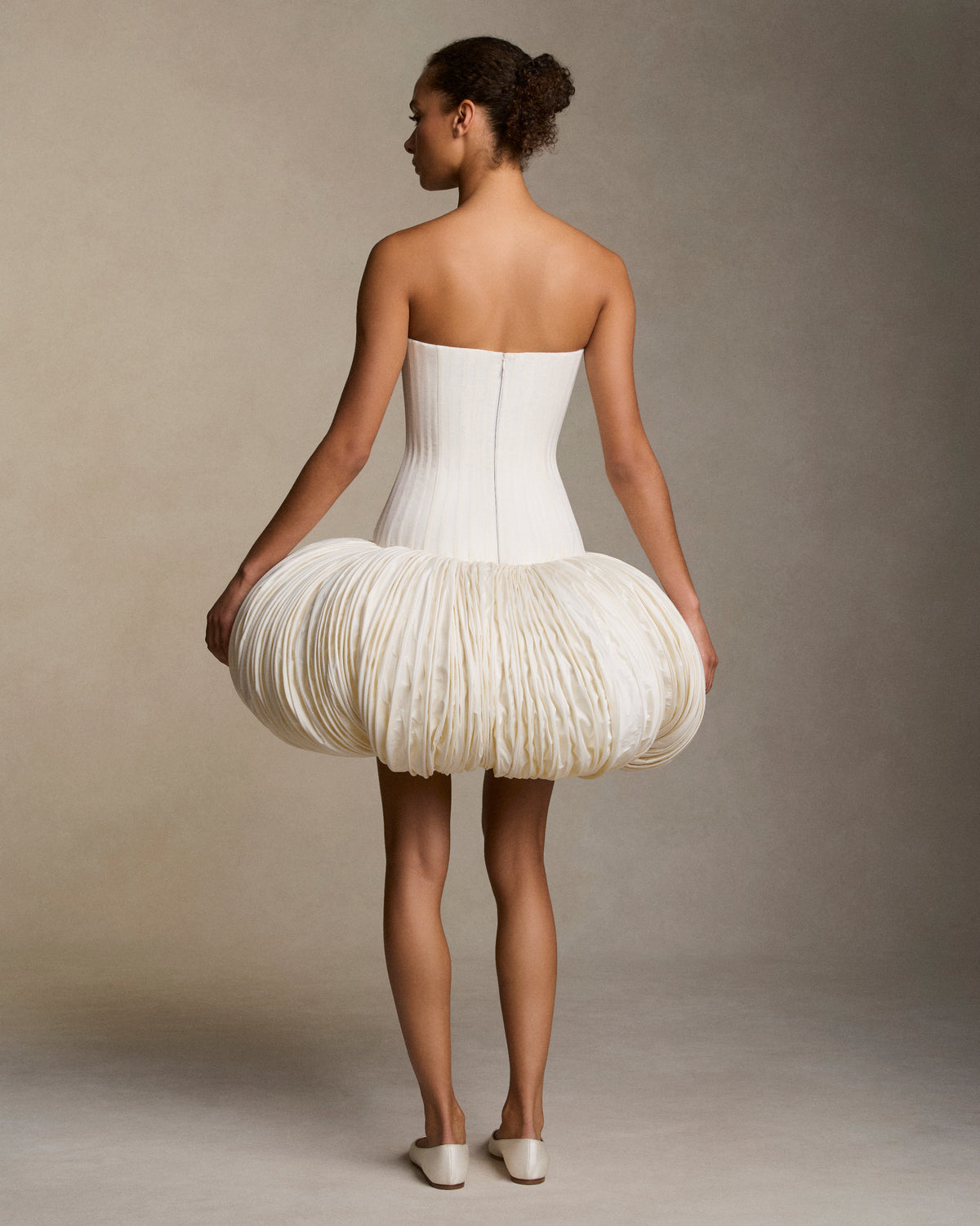 Strapless silk linen organza and tissue taffeta mini dress. Grosgrain boning detail throughout the linen organza bodice frames the silhouette. Exaggerated tissue taffeta bubble skirt is shaped with hundreds of rows of sculptural micro boning. Boned internal bustier, internal grosgrain belt and invisible zip closure at center back.
