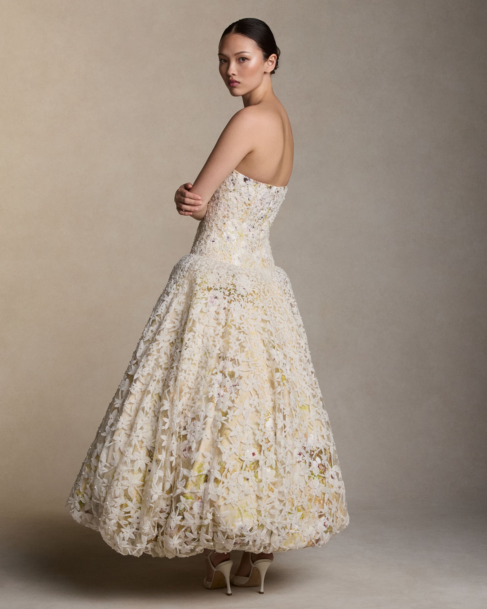 Strapless tea length ball gown with star flower pearl embroidery layered over hand painted silk wool satin. Thousands of hand cut silk chiffon petals with baroque pearls veil a layer of lustrous crinkled metal and silk. Interior lace-up corset with a grosgrain waist belt and double-zip bustier for added structure.