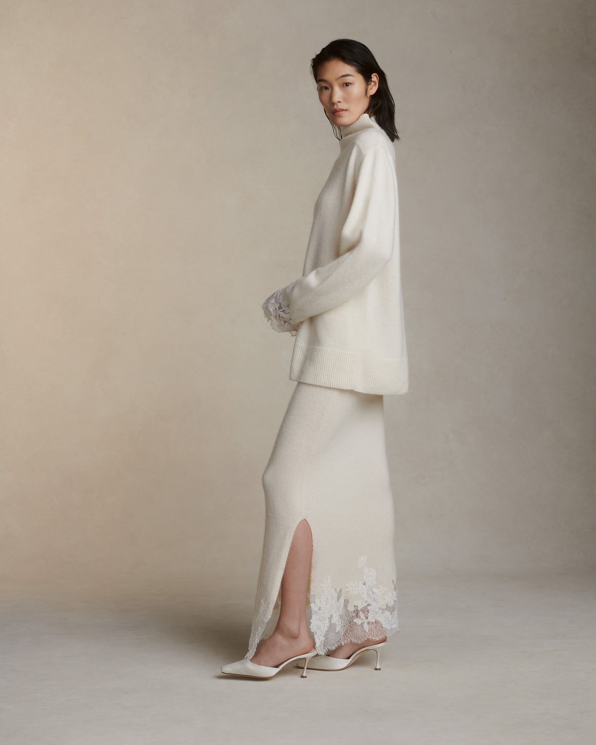 Silk cashmere knit pullover with hand cut chantilly and corded lace applique at sleeve opening. Angled high neck with rib knit sloped shoulder yoke. Side slits at sleeve opening. Rib knit hem.Styled with Viv skirt