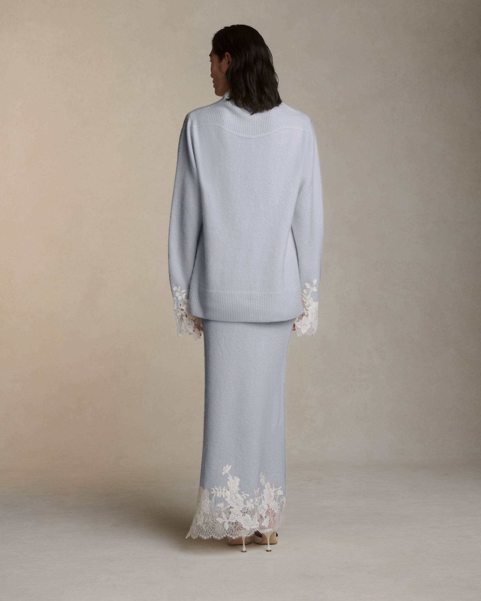 Silk cashmere knit pullover with hand cut chantilly and corded lace applique at sleeve opening. Angled high neck with rib knit sloped shoulder yoke. Side slits at sleeve opening. Rib knit hem.Styled with Viv skirt