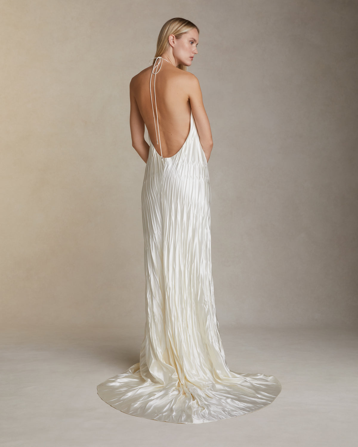 Pleated and hand crinkled silk wool halter neck gown. Spaghetti tie closure with baroque pearl cord end detail. Invisible zip closure at center back.