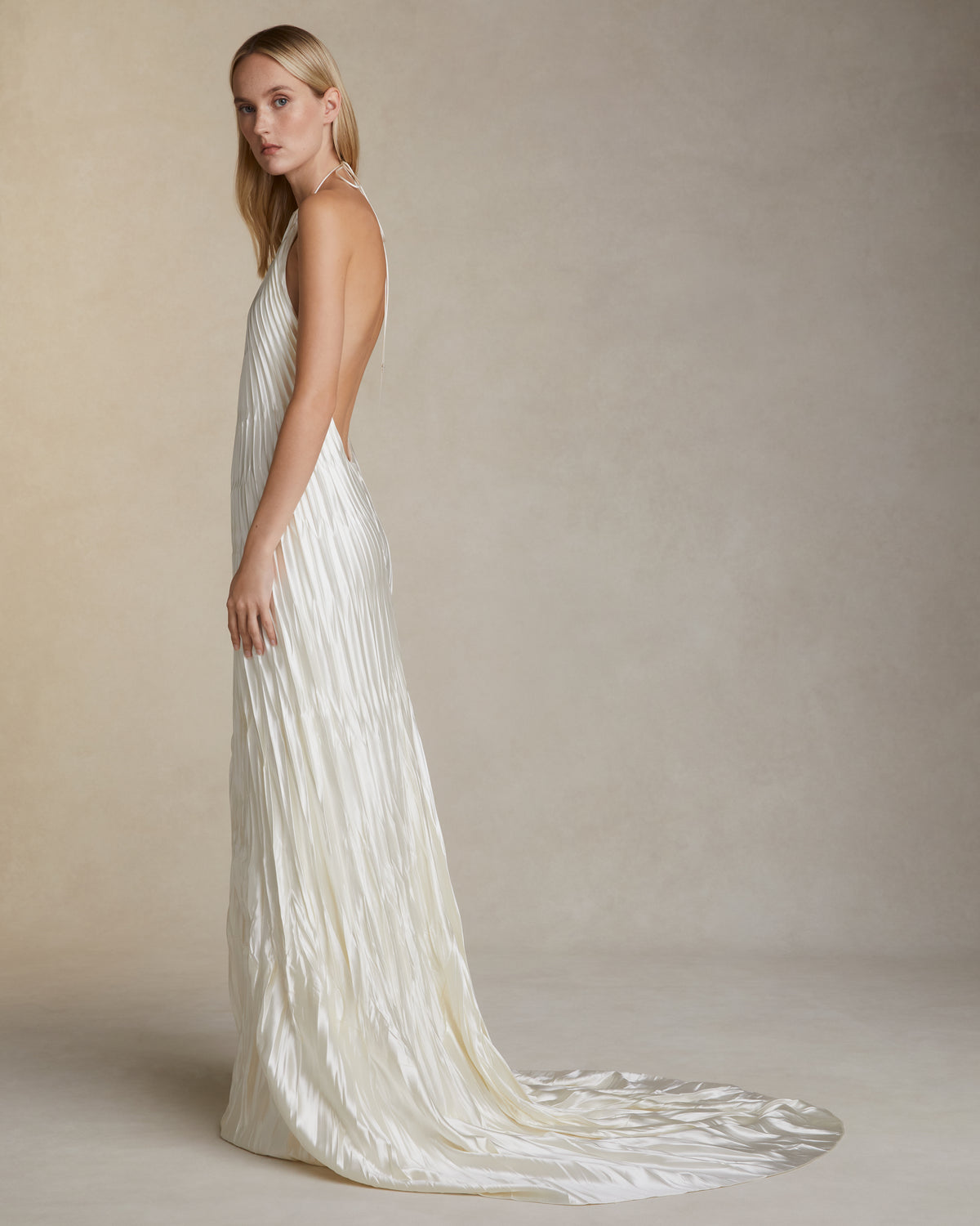Pleated and hand crinkled silk wool halter neck gown. Spaghetti tie closure with baroque pearl cord end detail. Invisible zip closure at center back.