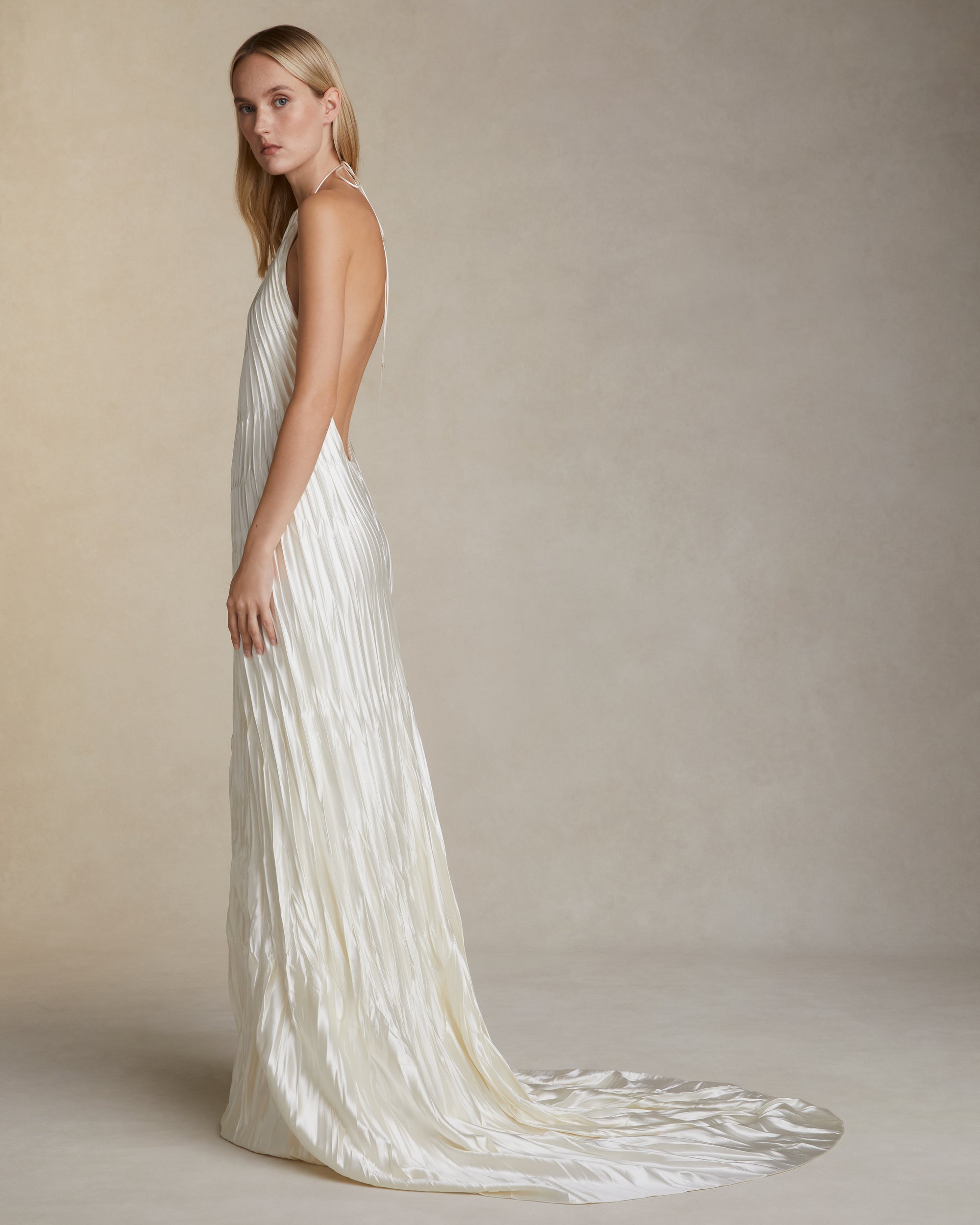 Pleated and hand crinkled silk wool halter neck gown. Spaghetti tie closure with baroque pearl cord end detail. Invisible zip closure at center back.