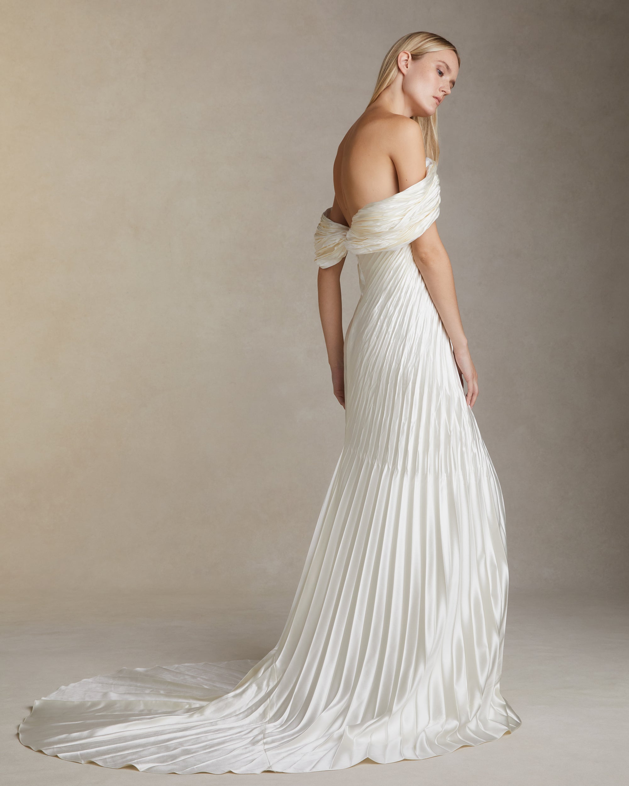 Off the shoulder pleated and hand crinkled silk wool gown with swagged sleeve drape releasing from center front neckline. Boned internal bustier, soft cups, internal grosgrain waist belt and invisible center back zip closure. 