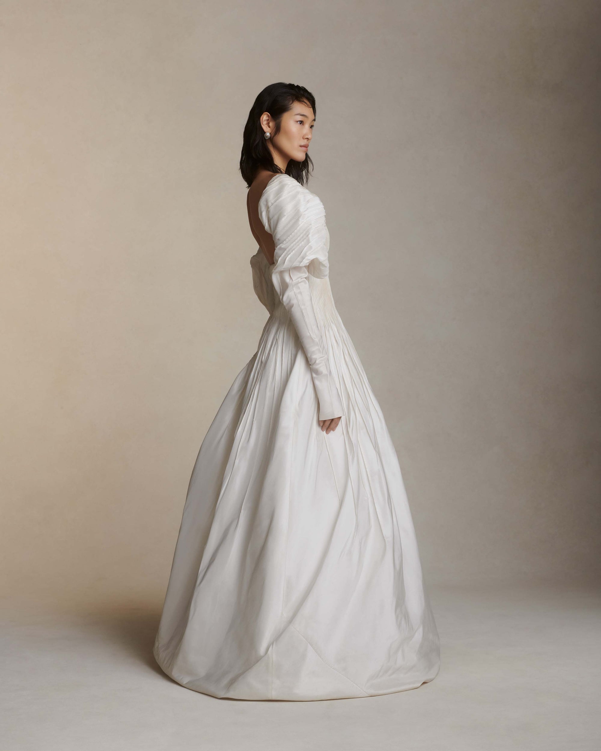 Tucked taffeta off the shoulder ball gown with crinoline encapsulated bubble hem. Boning and gummy tape at neckline for structure and security leading into draped, full length sleeves. Soft internal corset with wireless cups, grosgrain waistband with 3 position closure for support and external center back zipper. Organza and can can lined skirt for volume and hold. Available hand-dyed as editorial version $14990