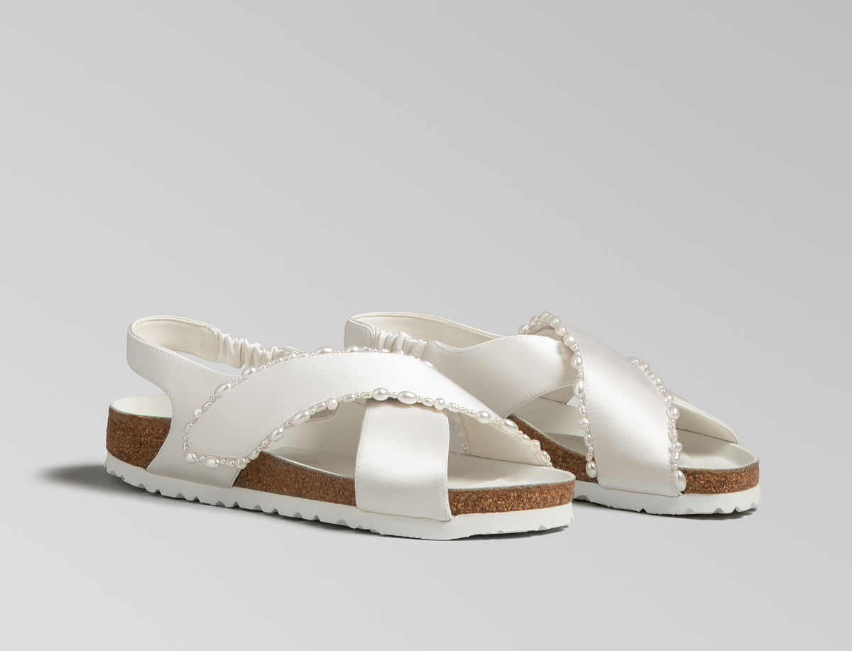 The Tulum is reimagined in a luminous ivory satin, featuring a graceful crossover profile and a slim ankle strap adorned with delicate pearls. The design also introduces an innovative adjustable hidden buckle closure. Handcrafted in Germany, the shoe merges BIRKENSTOCK’s legendary comfort with Danielle Frankel’s signature touch of refined elegance.- Upper: Delicate satin upper, naturally shaped pearls handstitched on trim- Footbed: Anatomical shaped BIRKENSTOCK cork latex Footbed lined with premium Nappa Leather- Sole: EVA die cut outsole with a custom design, blending classic BIRKENSTOCK bone pattern with delicate leaf inspired detailing